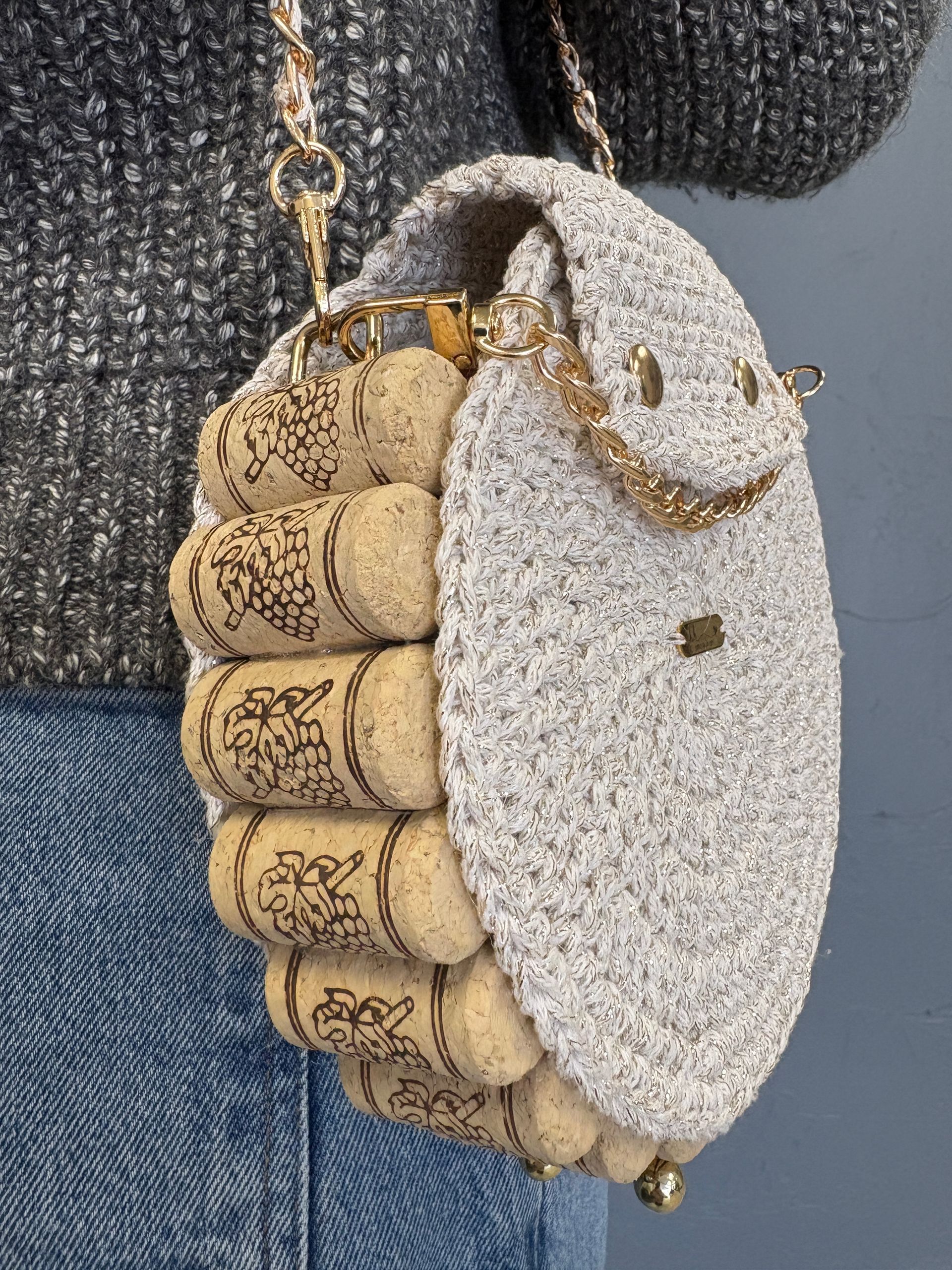 Woman wearing a unique purse made of wine corks and light gray fabric, with a gold chain strap.