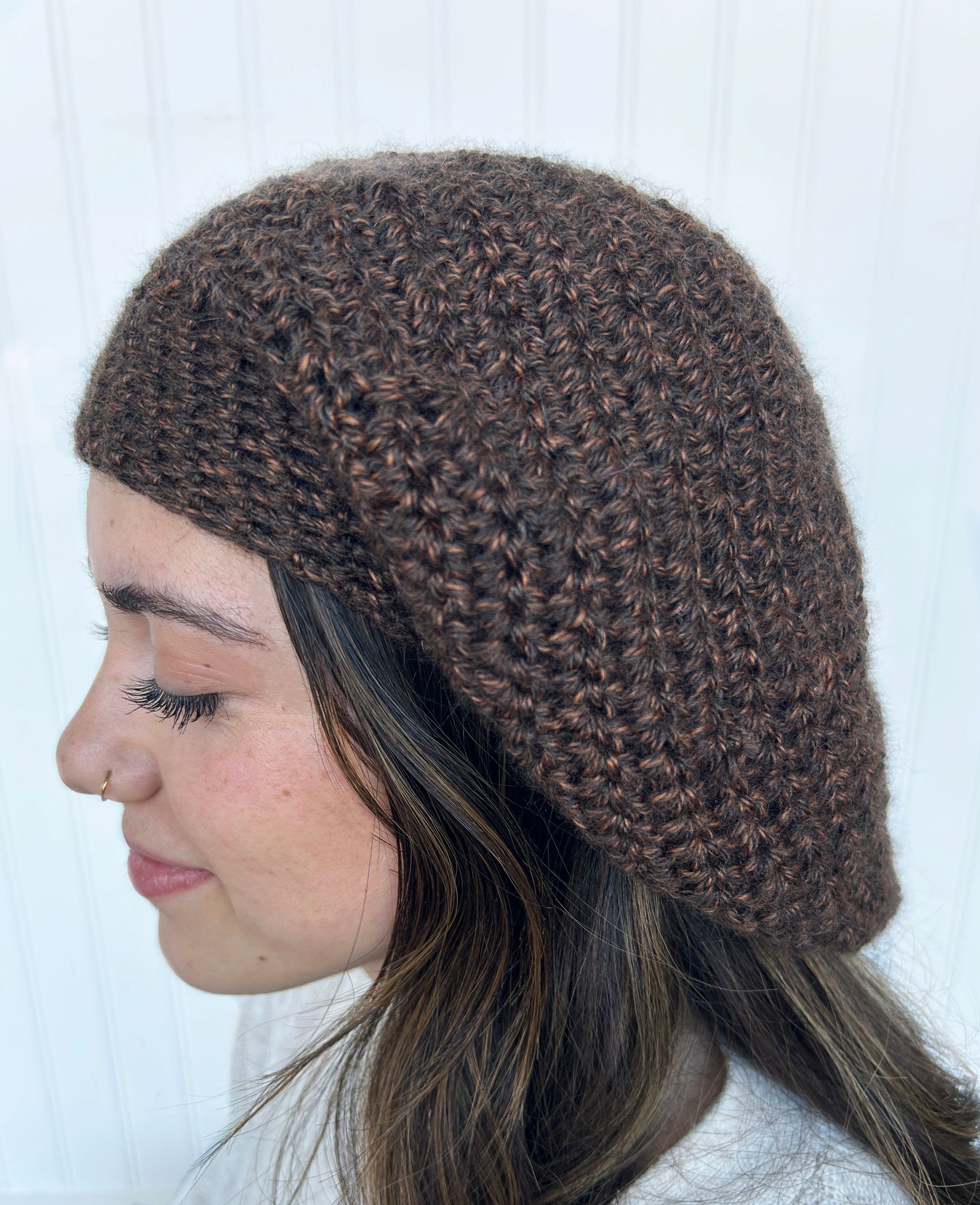 Woman wearing a dark brown knitted beret, side profile view.