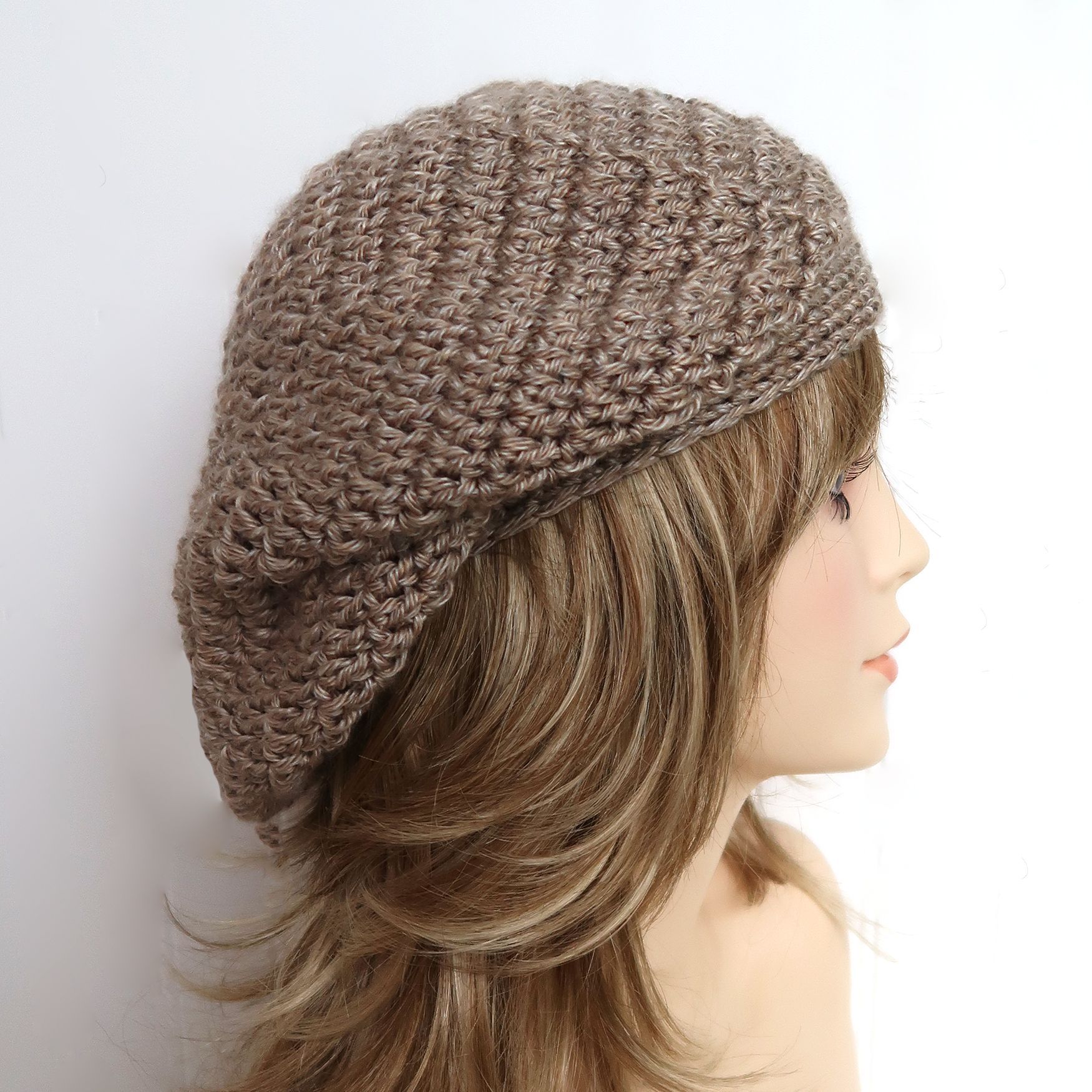 A woman wearing a tan crocheted beret, viewed in profile.
