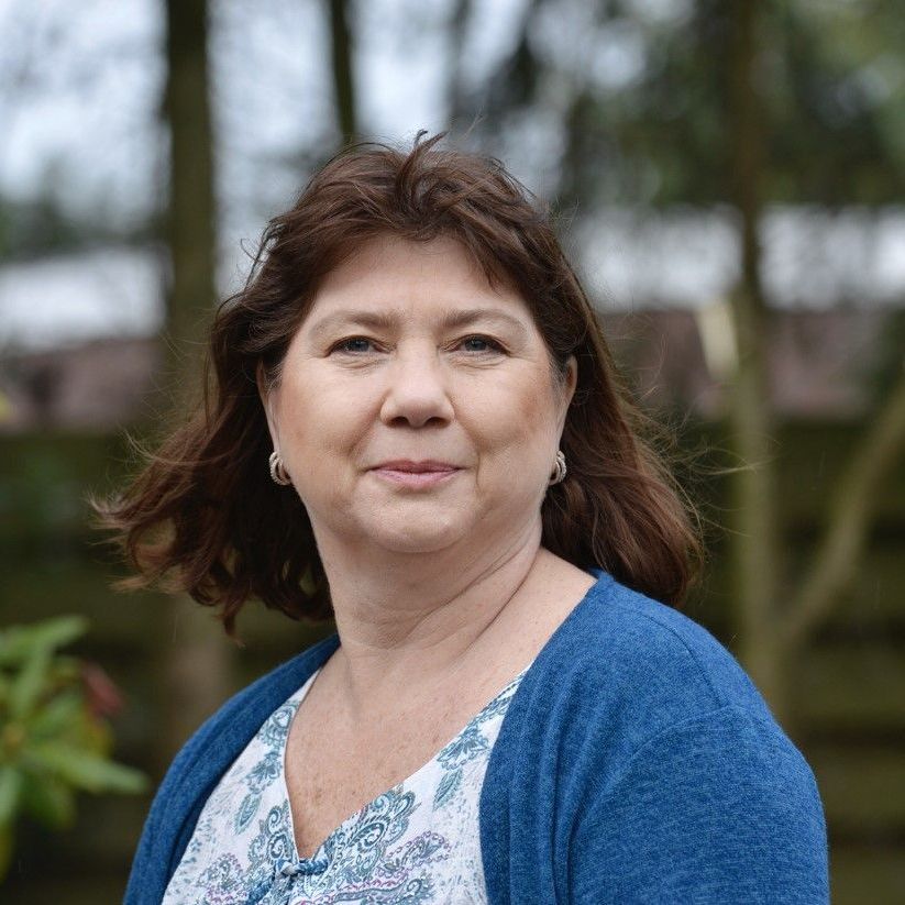 Een vrouw met een bril en een rood jasje lacht naar de camera.