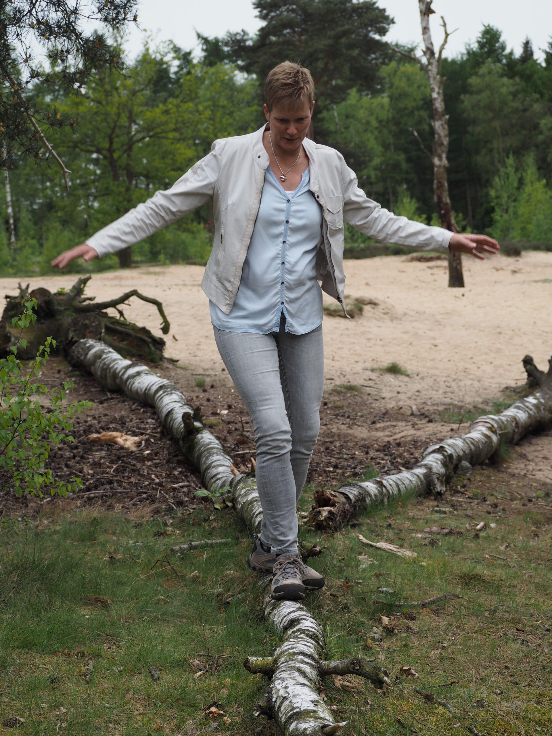 Een vrouw loopt op een boomstam in het bos.