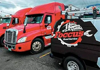 A row of red trucks parked next to a black van that says focus road service
