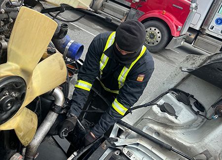 Mechanic in work clothes working on a truck engine, outdoors.