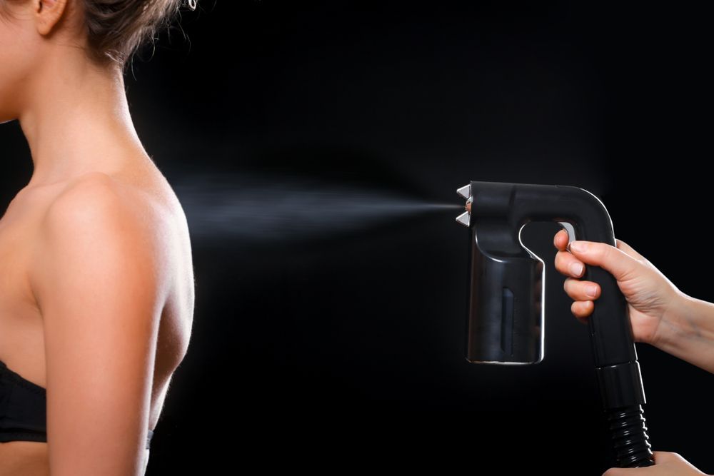 A Person Receiving a Spray Tan on Their Shoulder — Pink Lily Beauty in Blacksmiths, NSW