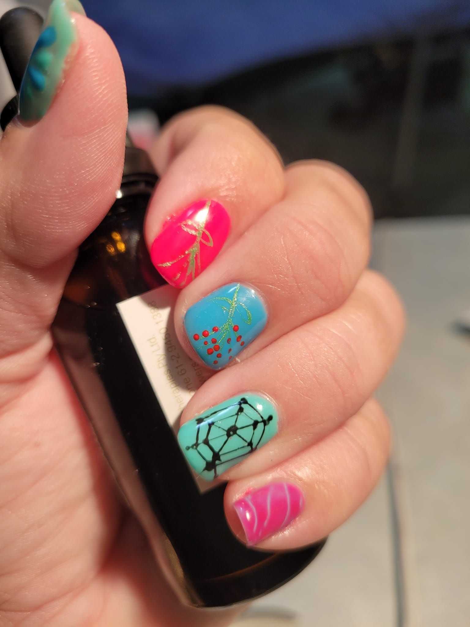 Hand with Colorful Nail Art Holding a Brown Bottle — Pink Lily Beauty in Blacksmiths, NSW