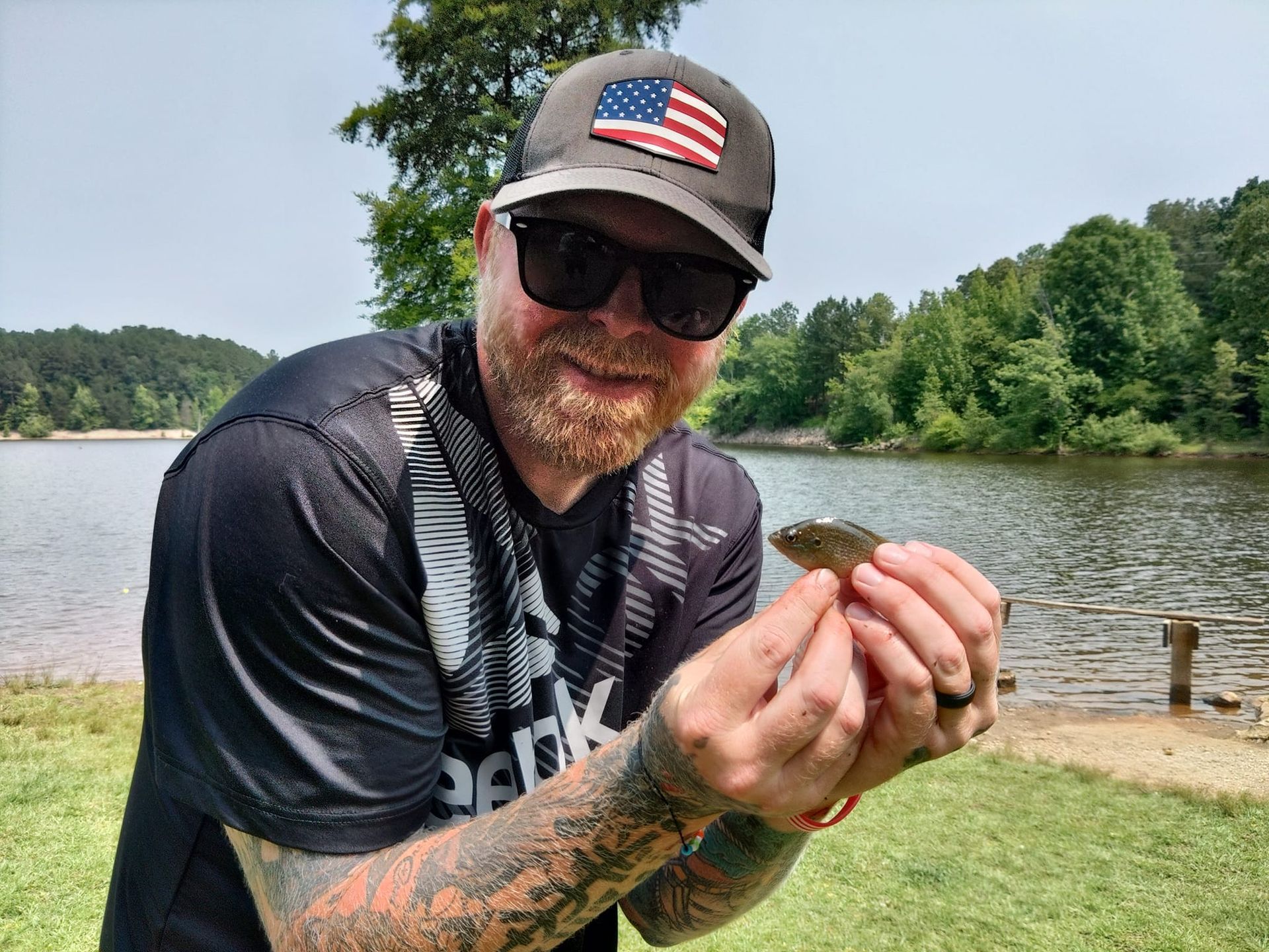 A man is holding a small fish in his hands in front of a lake.