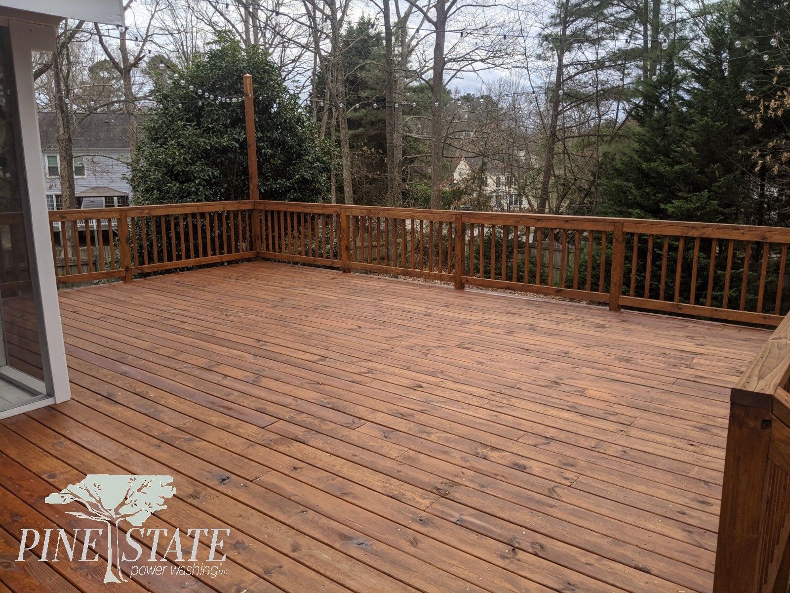 A large wooden deck with a wooden railing and trees in the background.