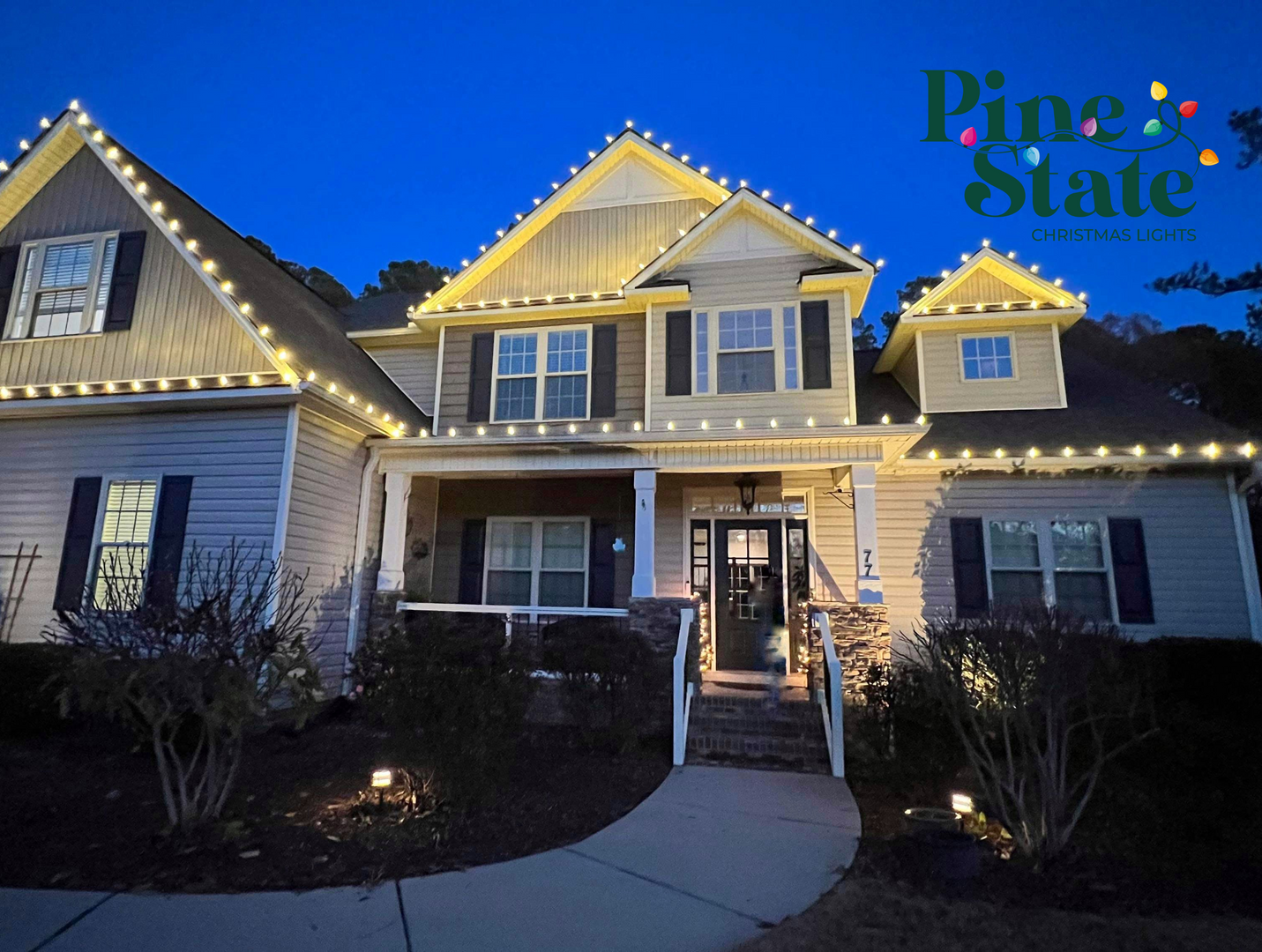 A large two-story house at dusk, decorated with bright white roofline holiday lights and featuring a lit front entryway.