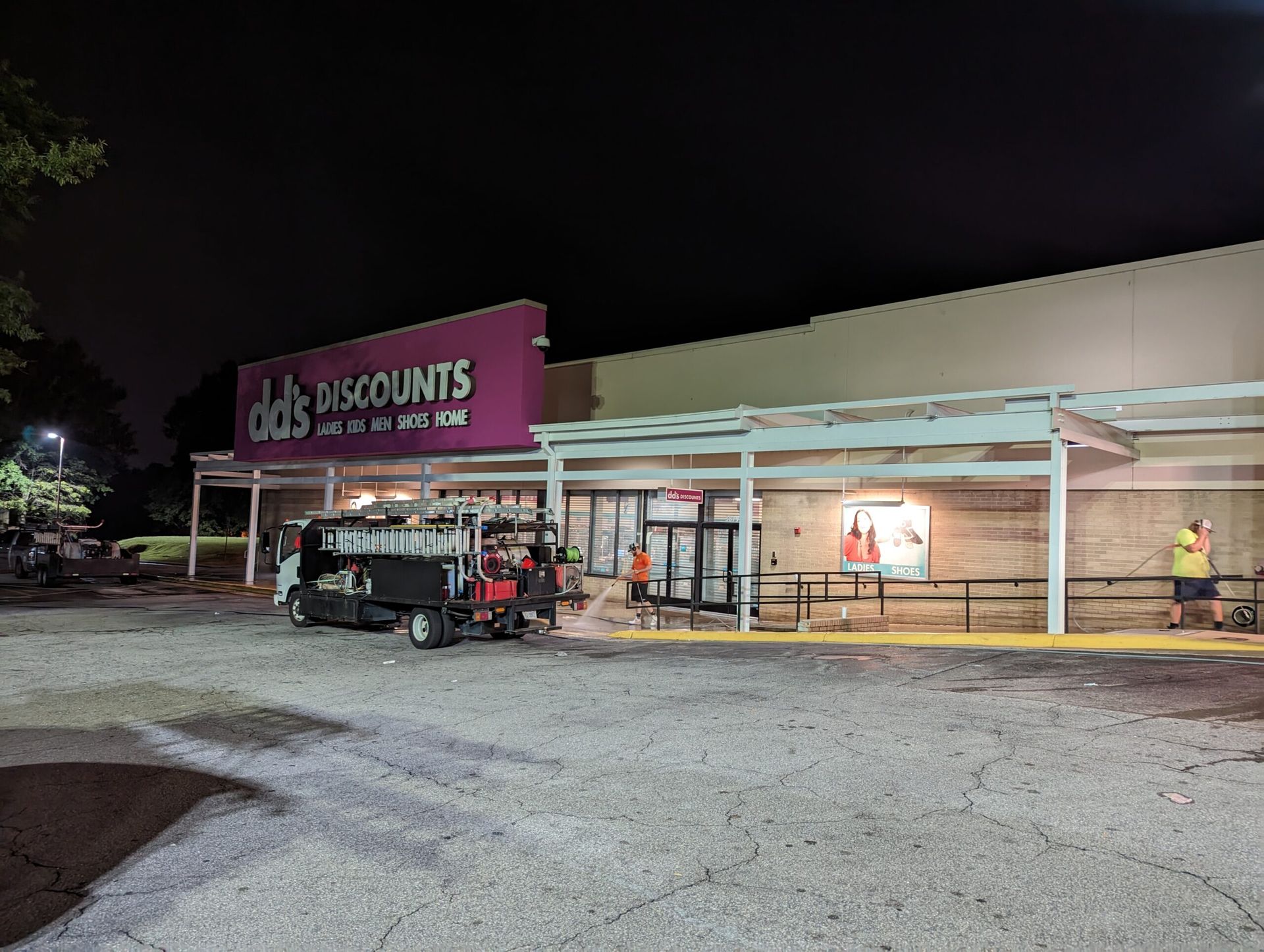 A dd's Discounts store at night with a utility vehicle parked in front and individuals working on the storefront.
