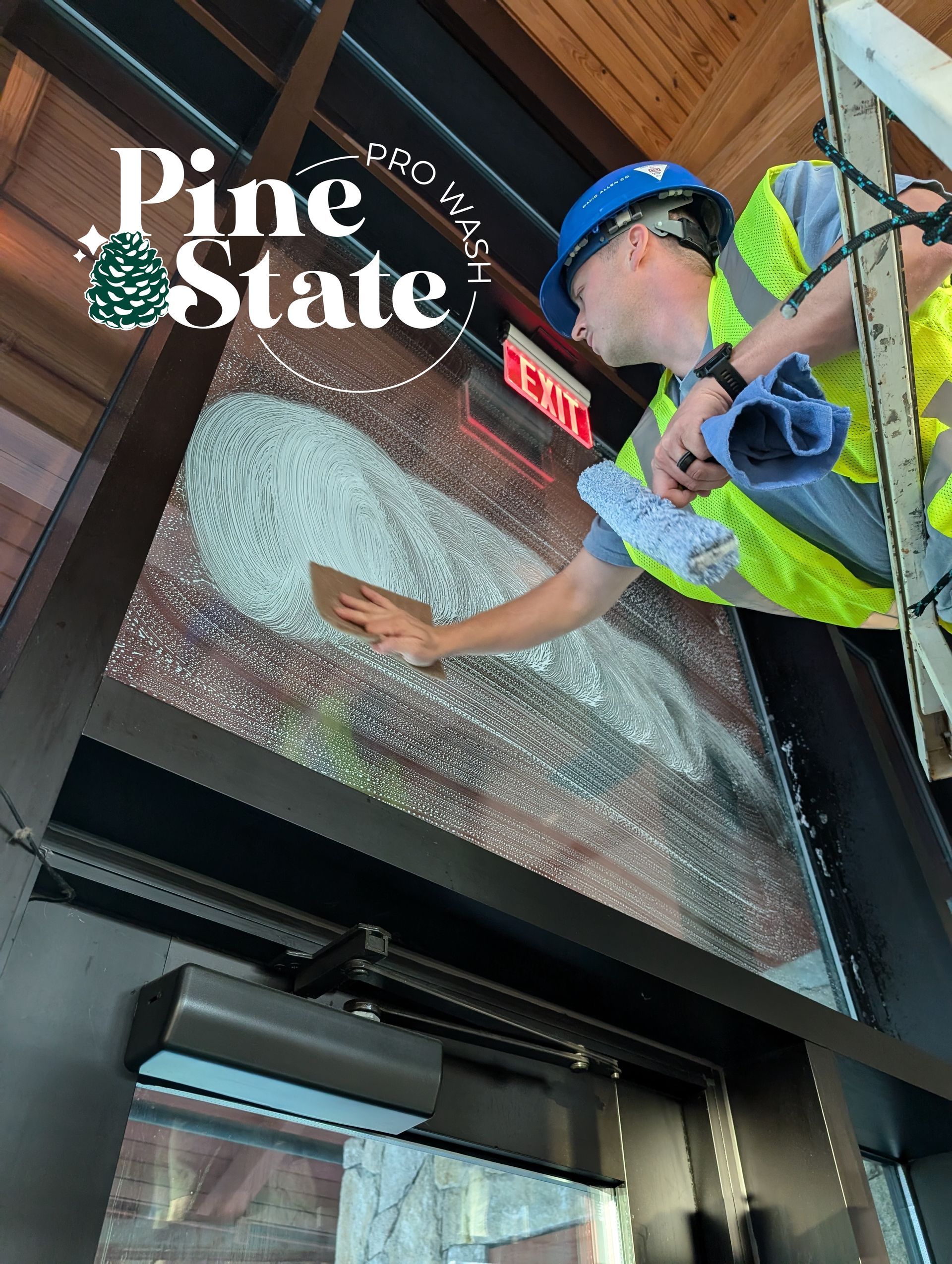 A worker in a high-visibility vest and blue hard hat installs window film on a door with a Pine State logo overlay.