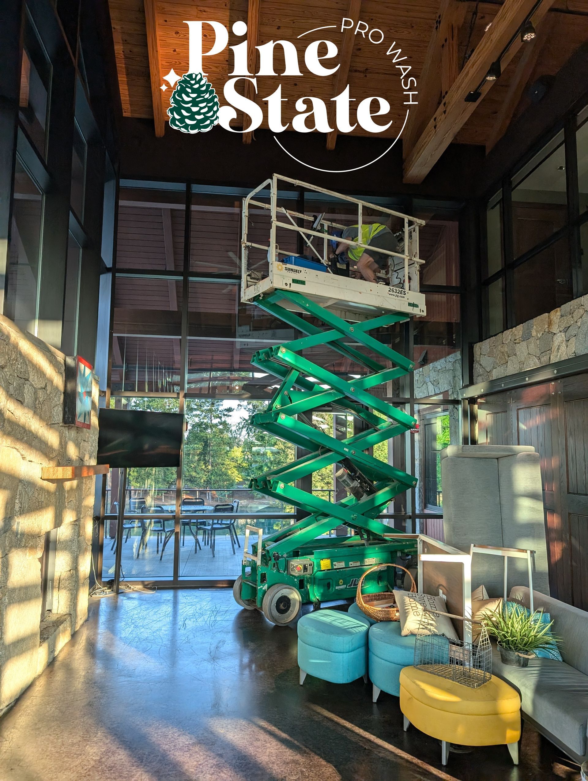 A green scissor lift stands in a bright lobby with stone walls, light-blue ottomans, and a yellow seat.
