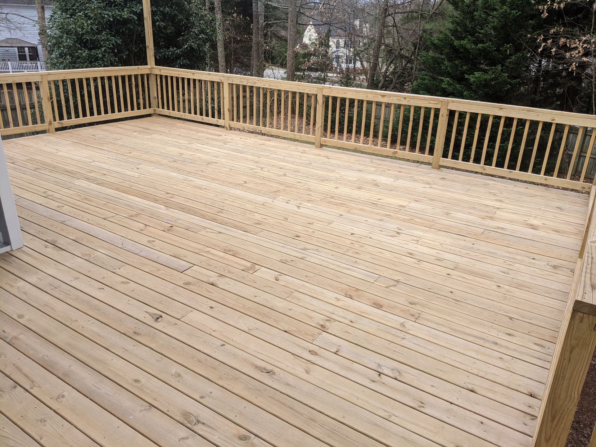 A large wooden deck with a railing and trees in the background
