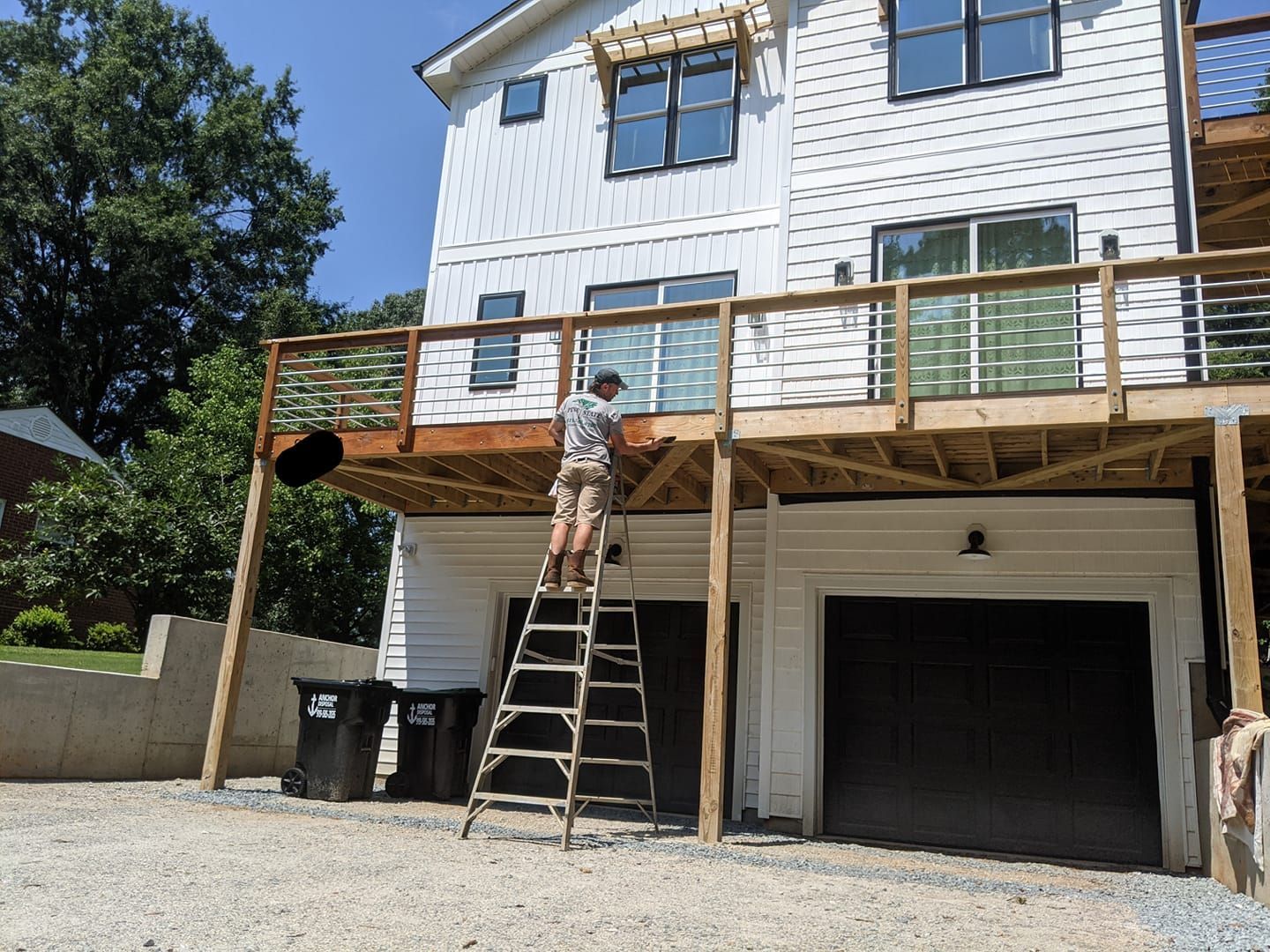 A man is standing on a ladder on a deck in front of a house.