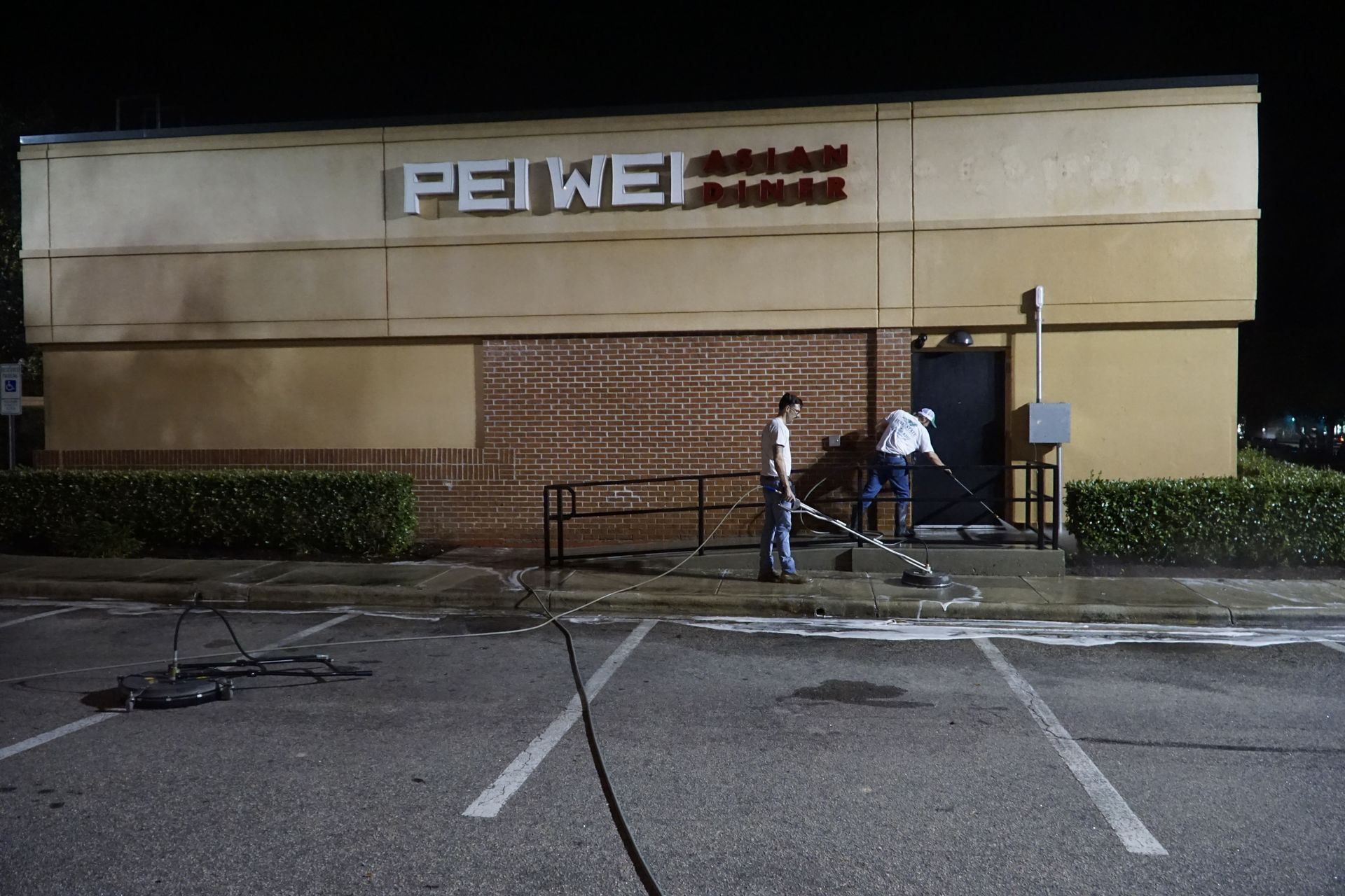 Two men are cleaning the outside of a pei wei restaurant at night