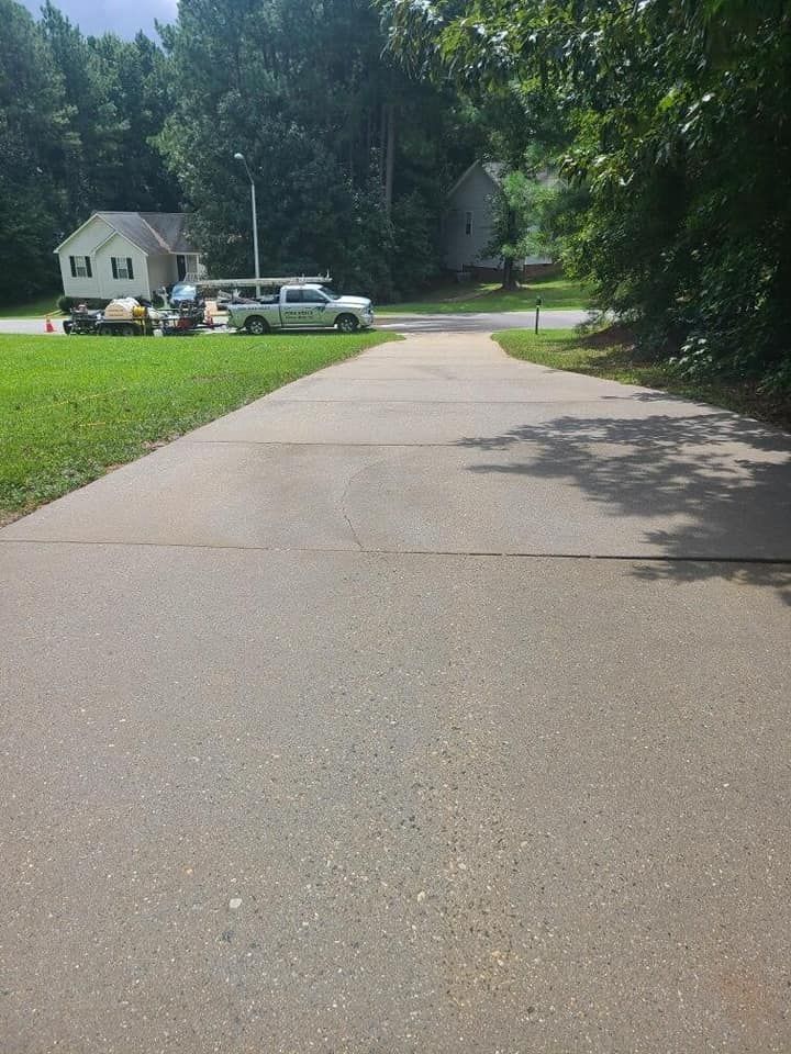 A paved driveway leading toward a residential street with a house and a light-colored pickup truck in the background.