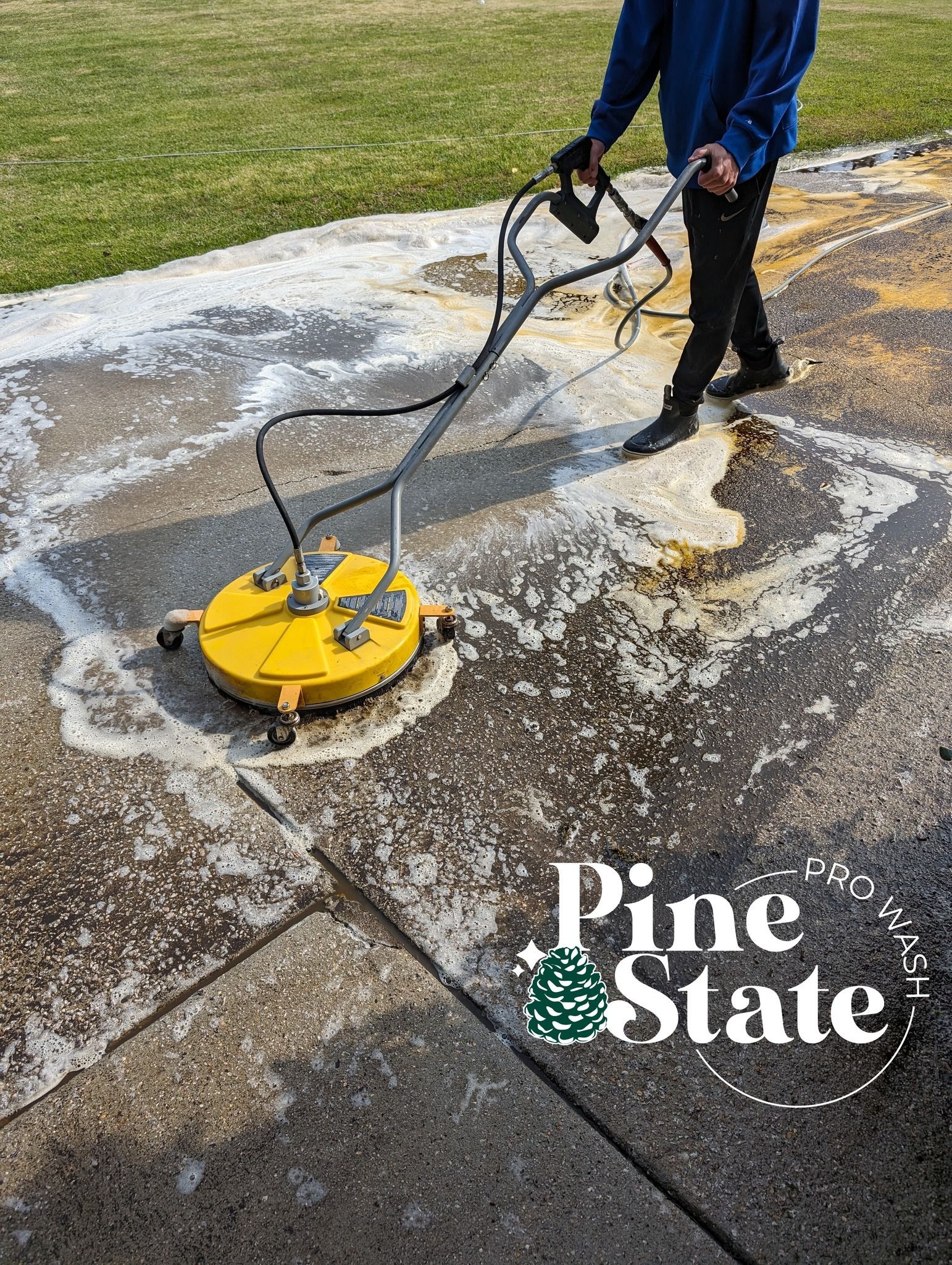 A person using a yellow circular surface cleaner on a dirty concrete patio outdoors, with a Pine State logo overlay.