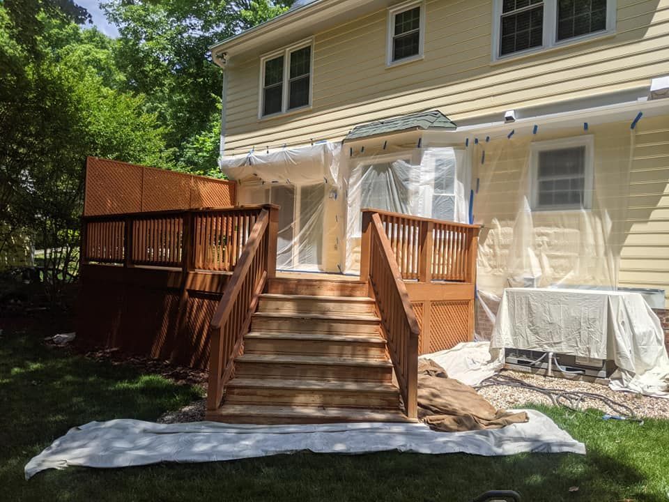 A wooden deck is being painted in front of a house.