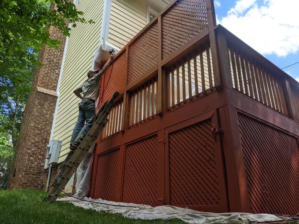 A man is standing on a ladder painting the side of a house.