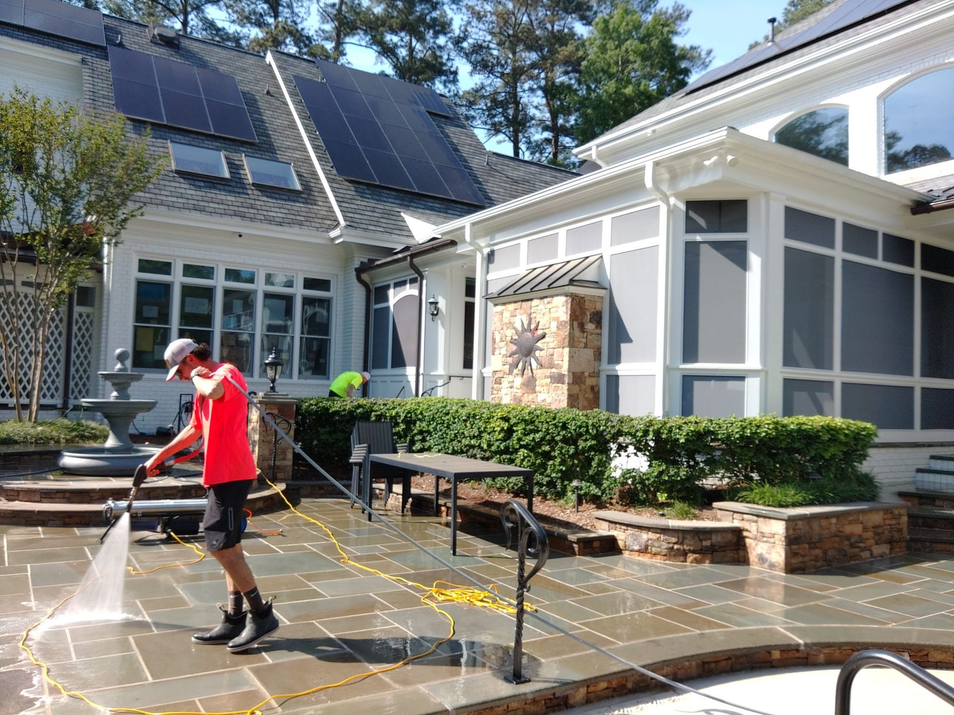 A man is cleaning a patio with a pressure washer in front of a house.