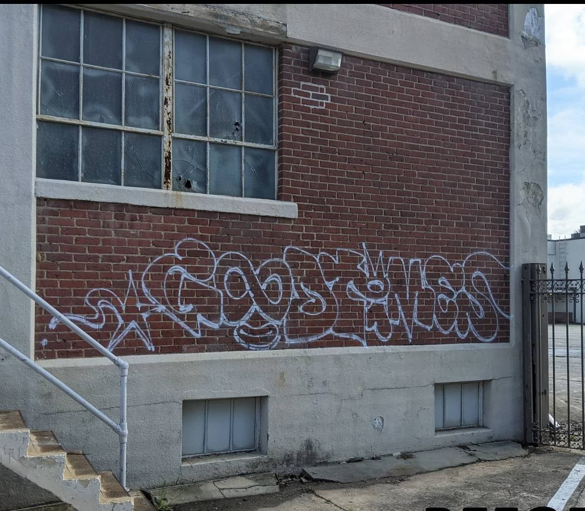 White graffiti tagging in a stylized, cursive script on a red brick wall of a building exterior.