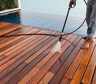 A person power washing a wooden deck next to a pool.