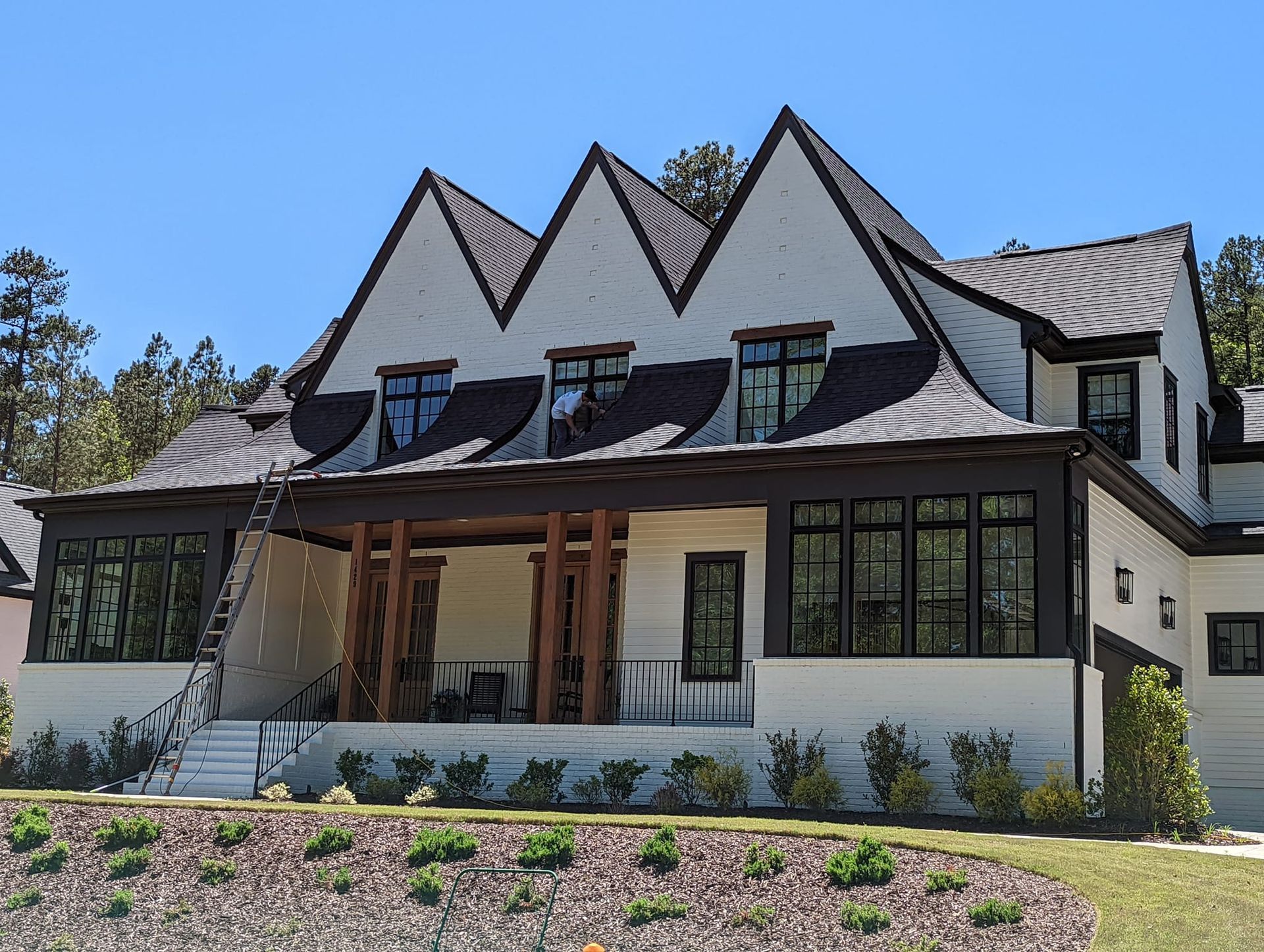 A modern two-story home with triple gables, white brick exterior, dark window frames, and a spacious front porch.
