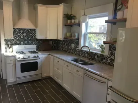 A kitchen with white cabinets , a stove , a sink , and a refrigerator.
