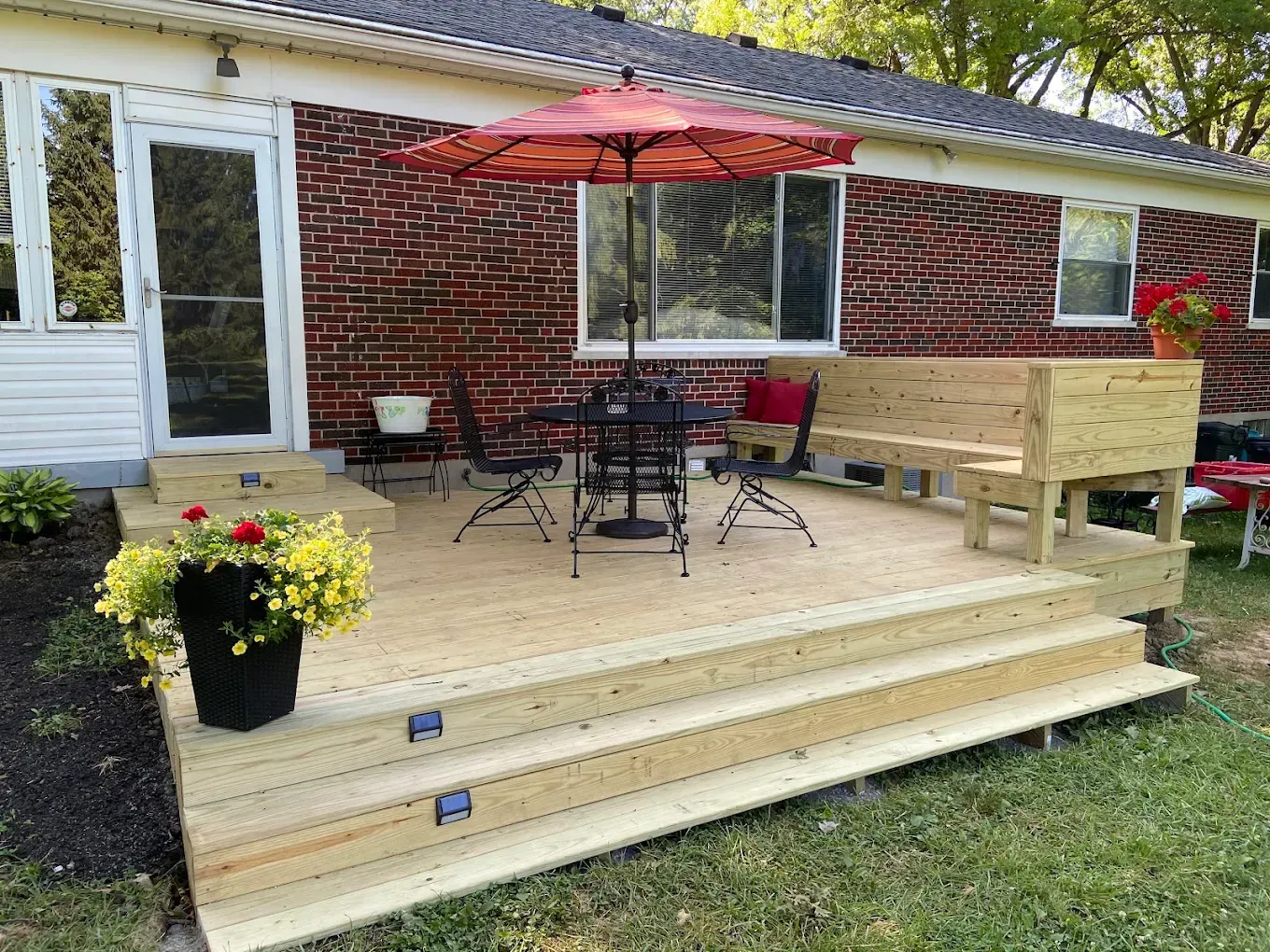 A wooden deck with a table and chairs and an umbrella in front of a brick house.
