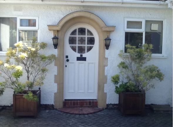 A white door with a round window is surrounded by potted plants
