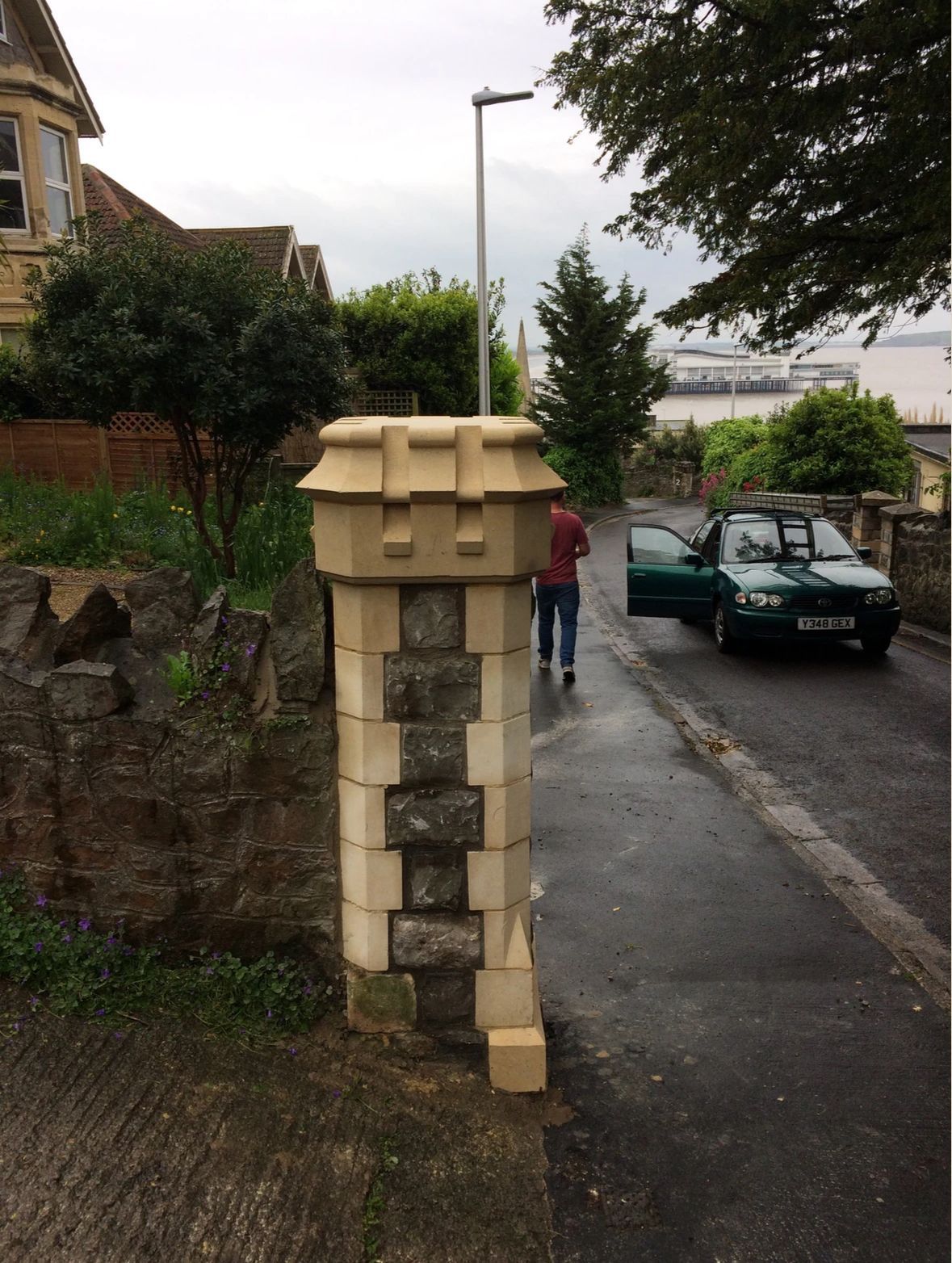 A green car is parked on the side of the road next to a stone pillar
