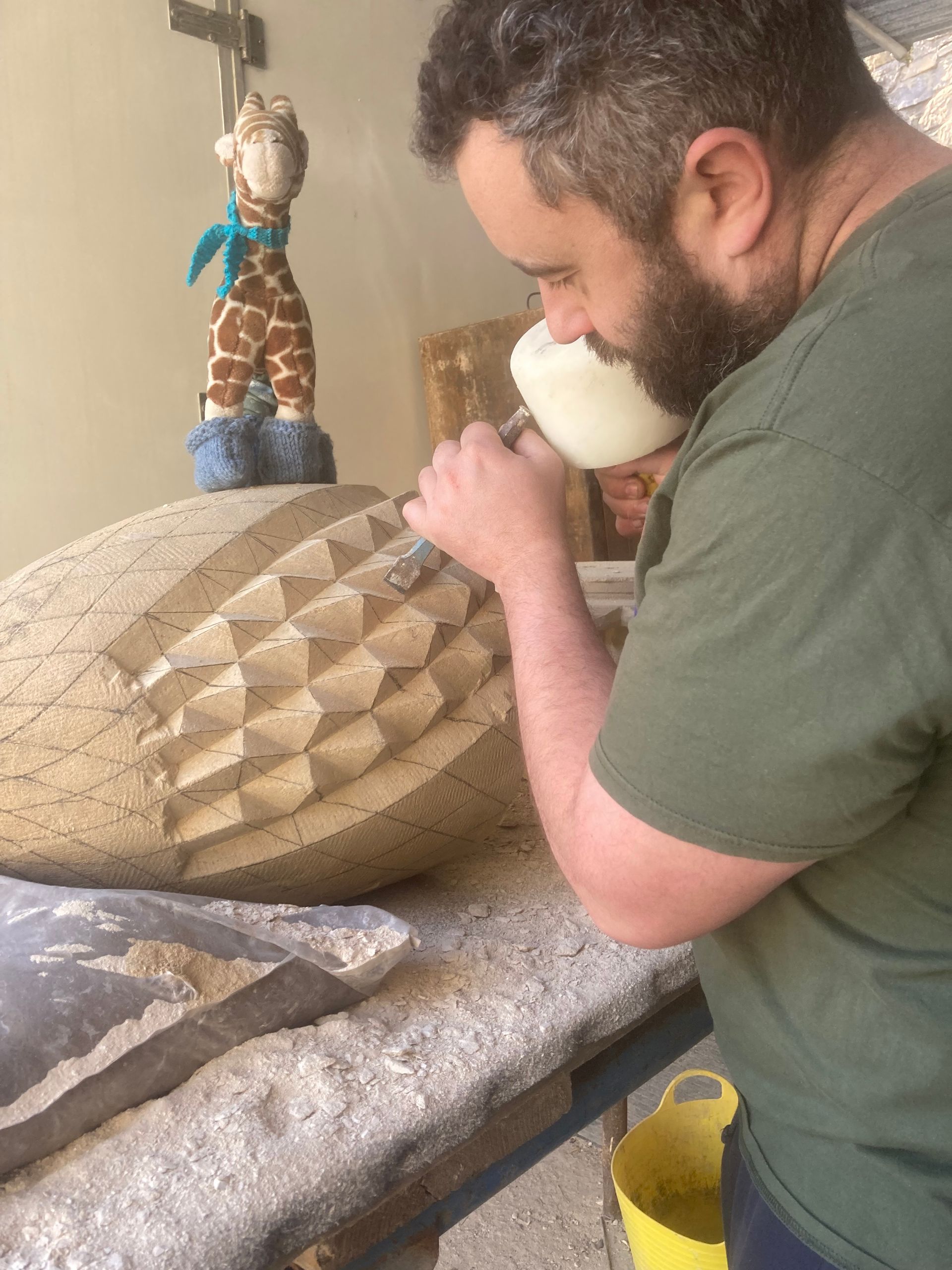 A man with a beard is carving a sculpture on a table.