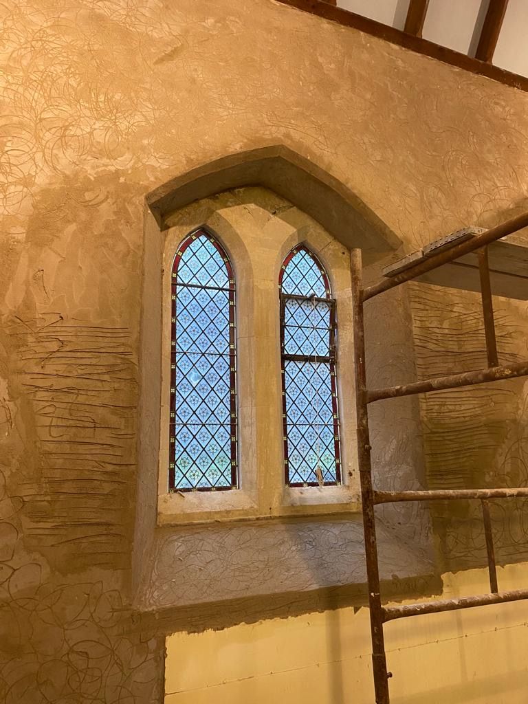 A stained glass window in a building with a ladder in the background.