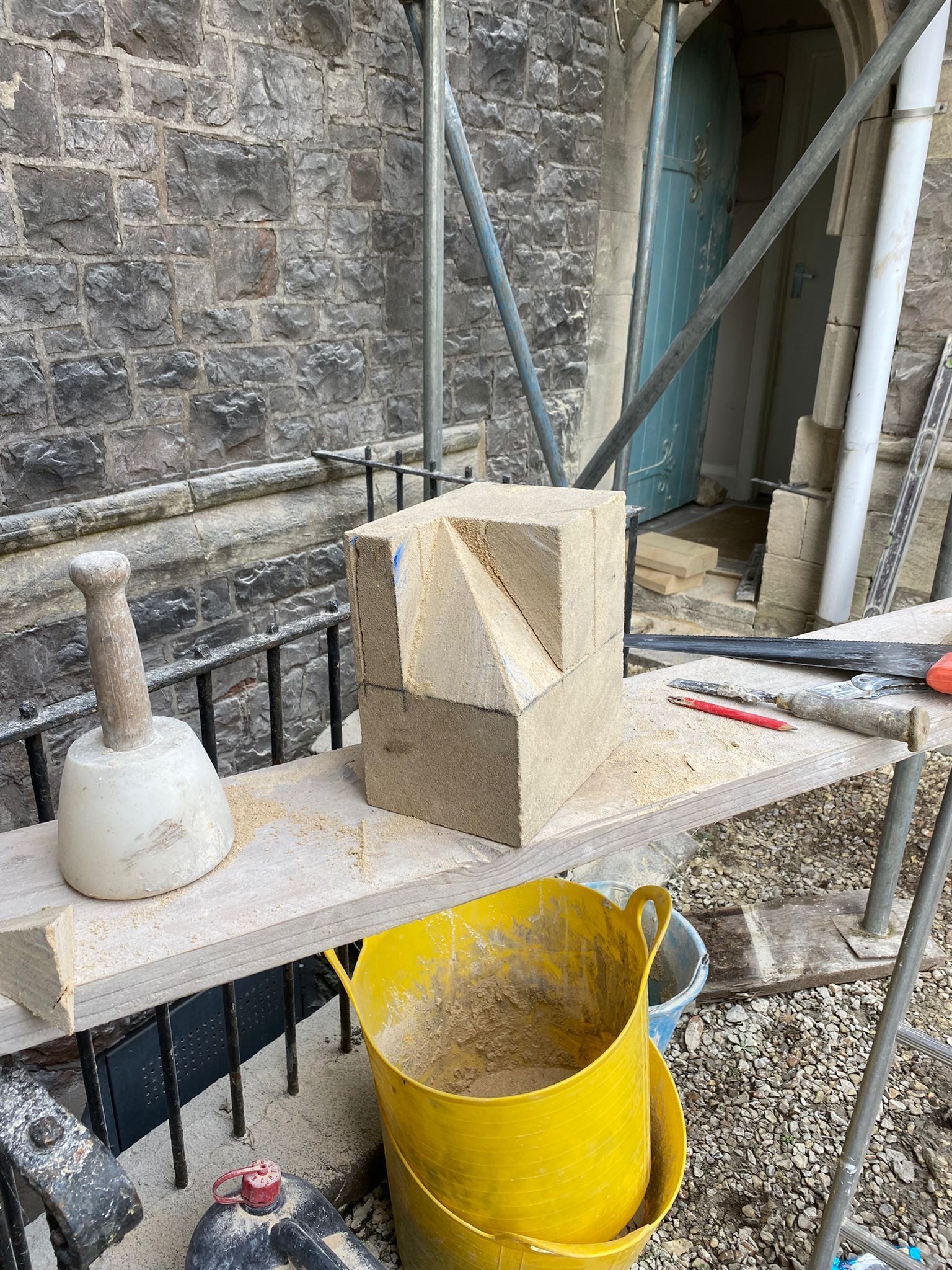 A brick is sitting on top of a wooden shelf next to a yellow bucket.