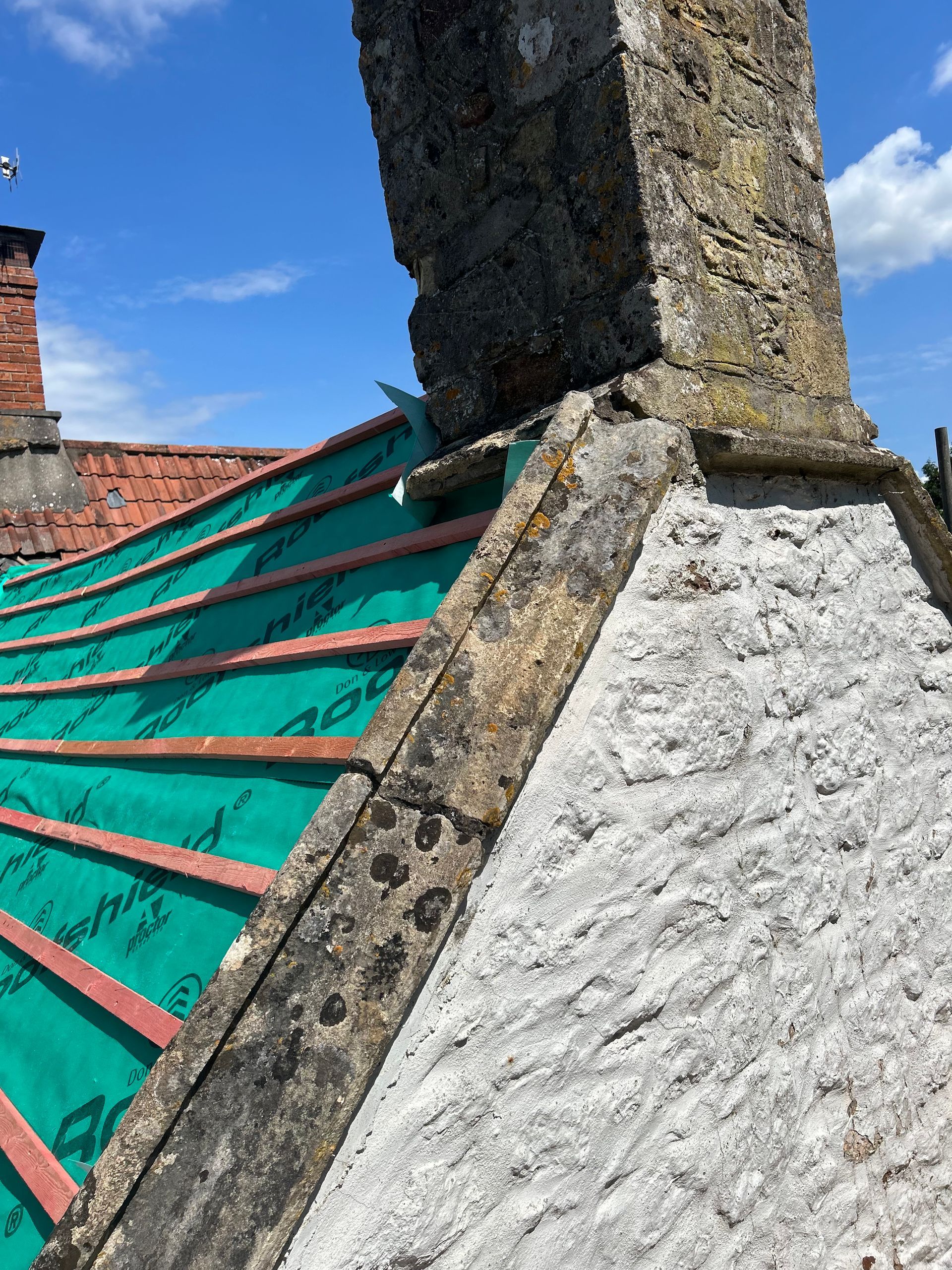 A roof with a chimney and a green tarp on it.