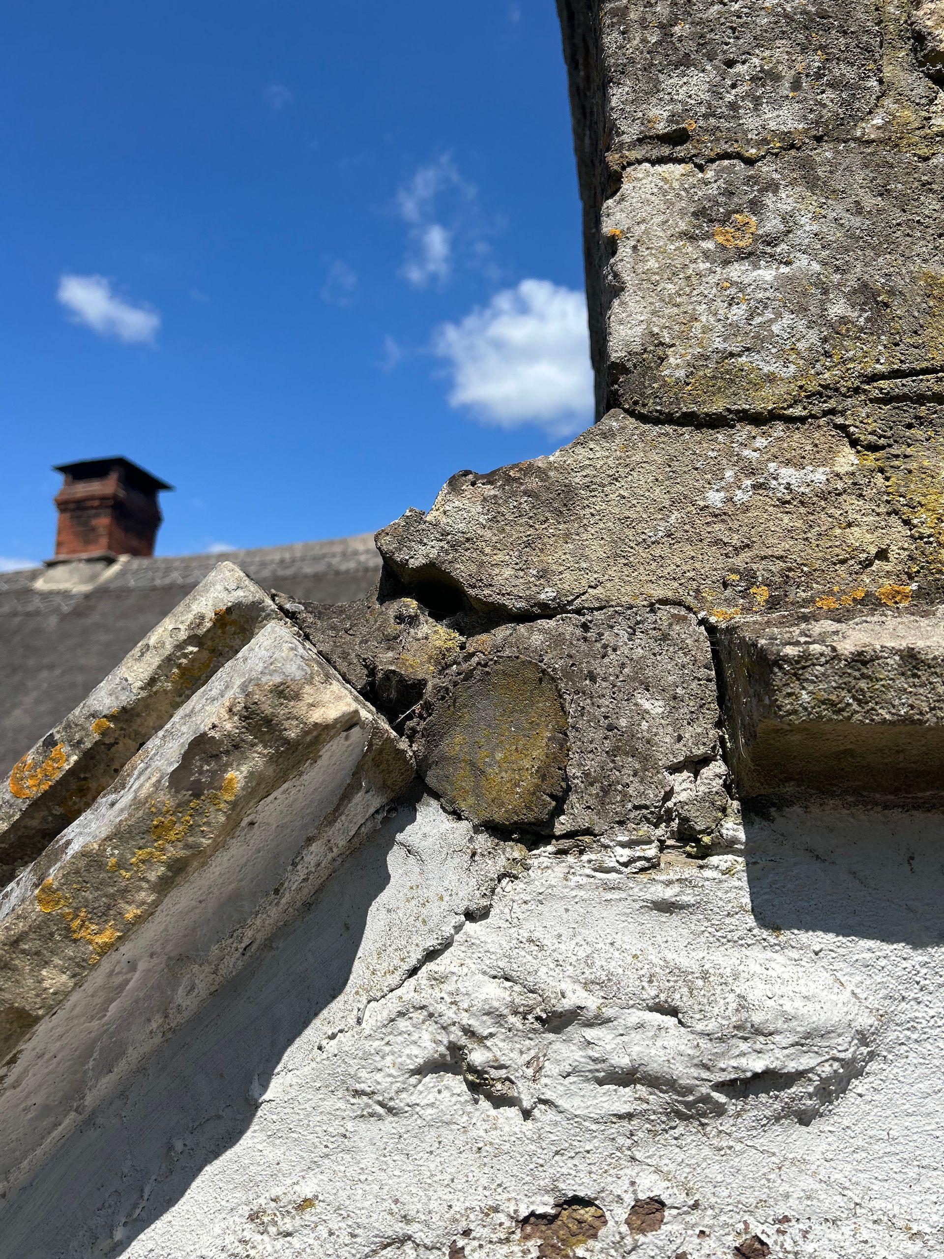 A broken stone wall with a chimney in the background.