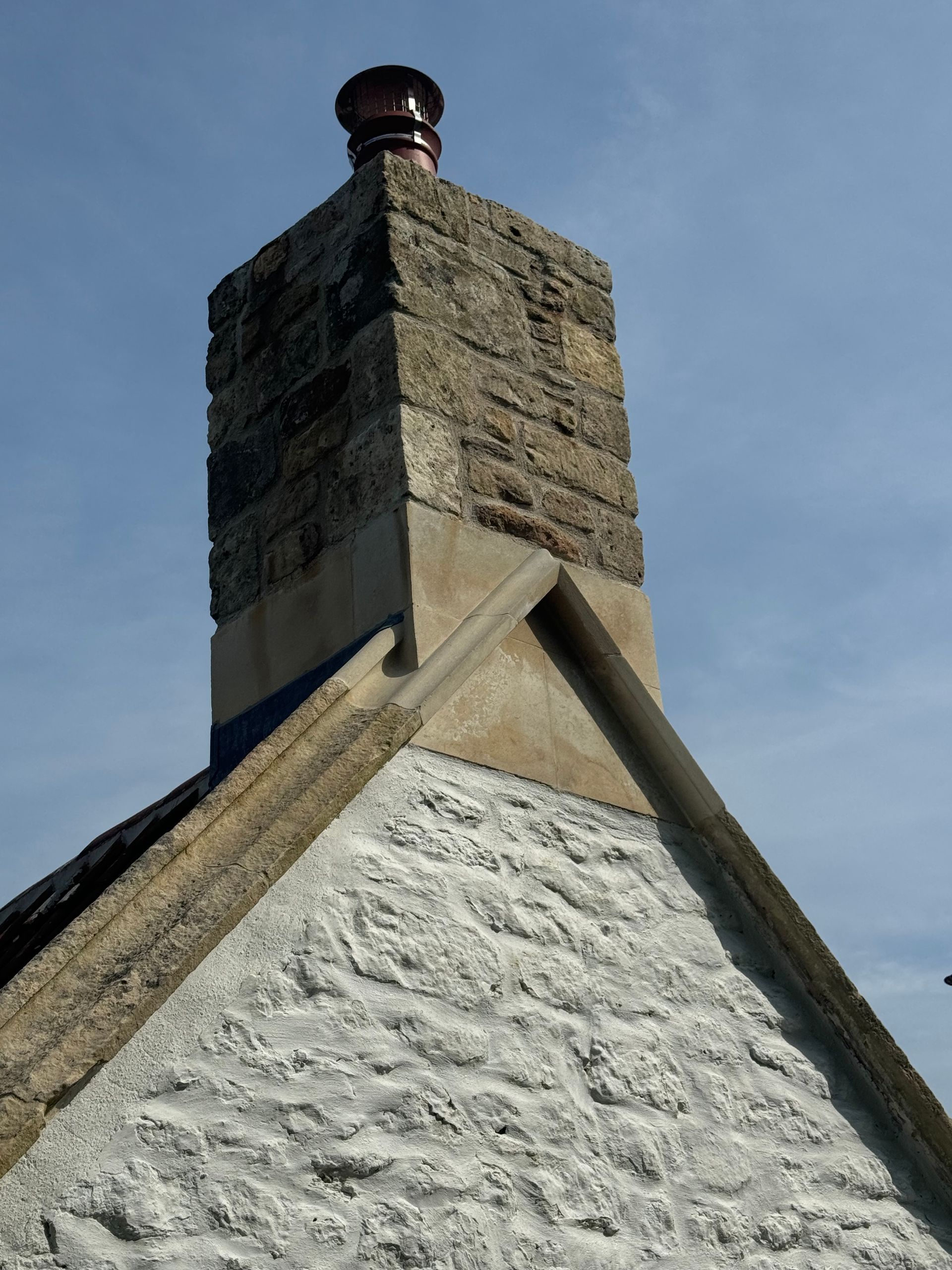 A chimney on top of a stone building with a blue sky in the background