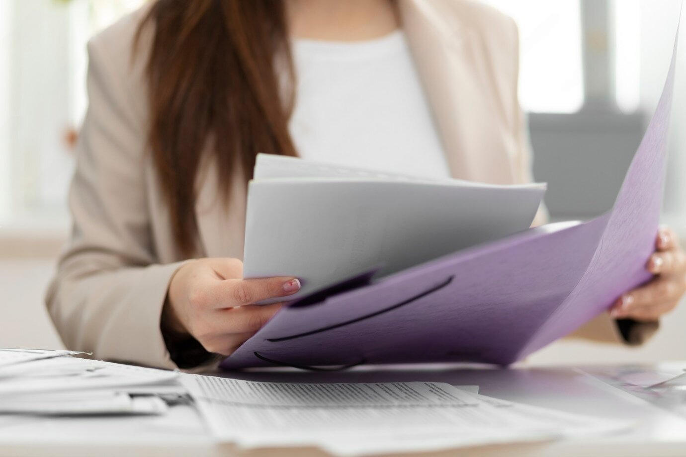 Una mujer está sentada en un escritorio sosteniendo una carpeta violeta y una hoja de papel.