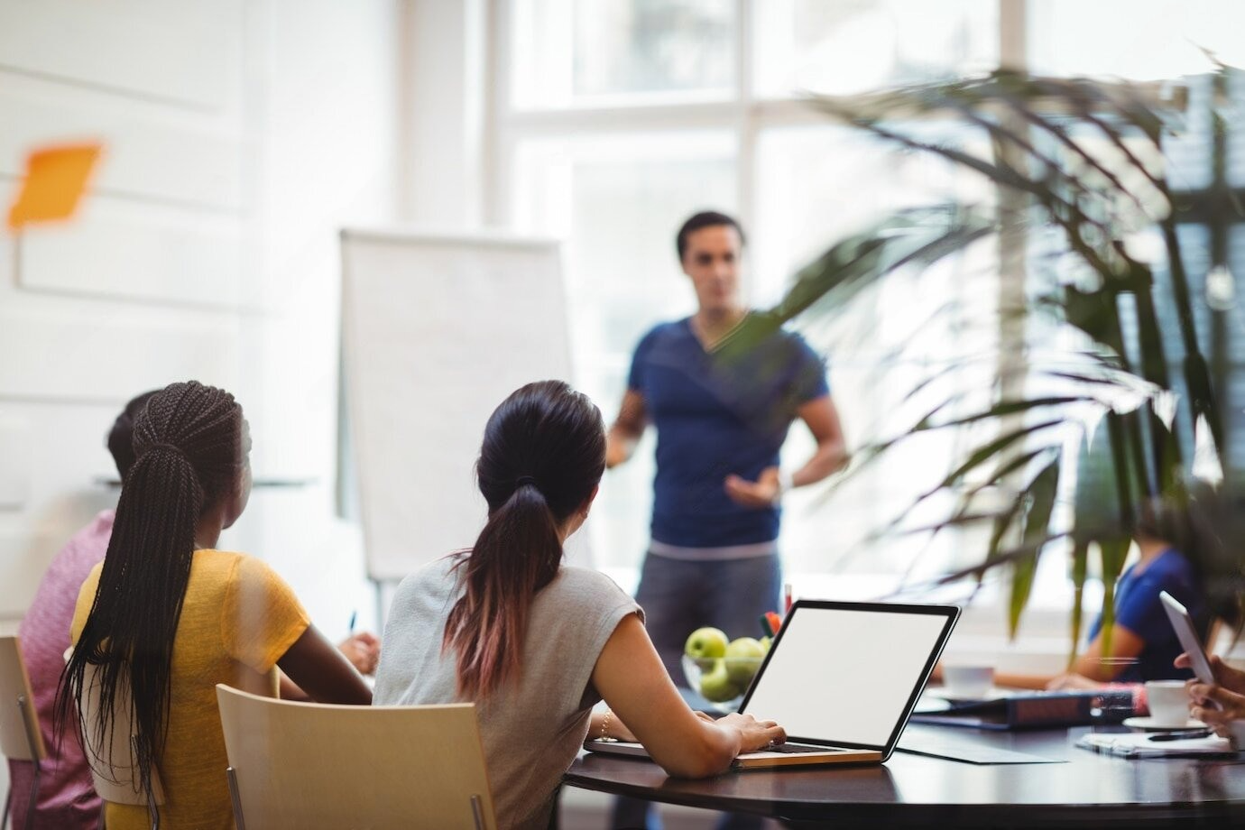 Un grupo de personas está sentada en una mesa con computadoras portátiles y un hombre está haciendo una presentación.