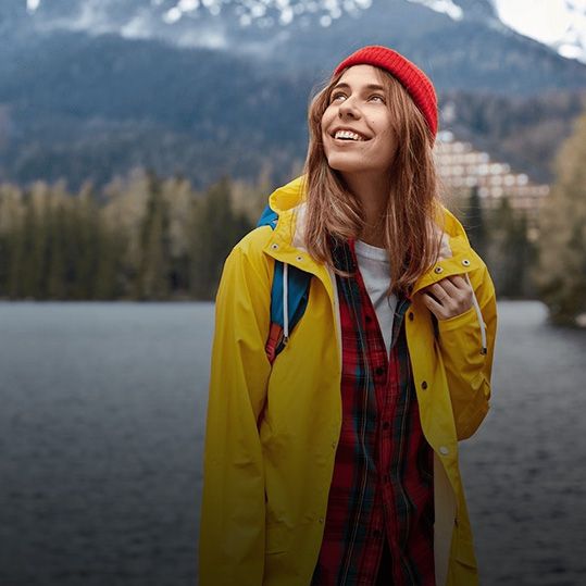 Una mujer con una chaqueta amarilla y un sombrero rojo está parada junto a un lago.