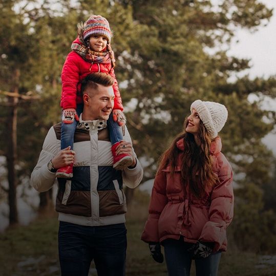 Un hombre lleva a un niño sobre sus hombros mientras una mujer observa.