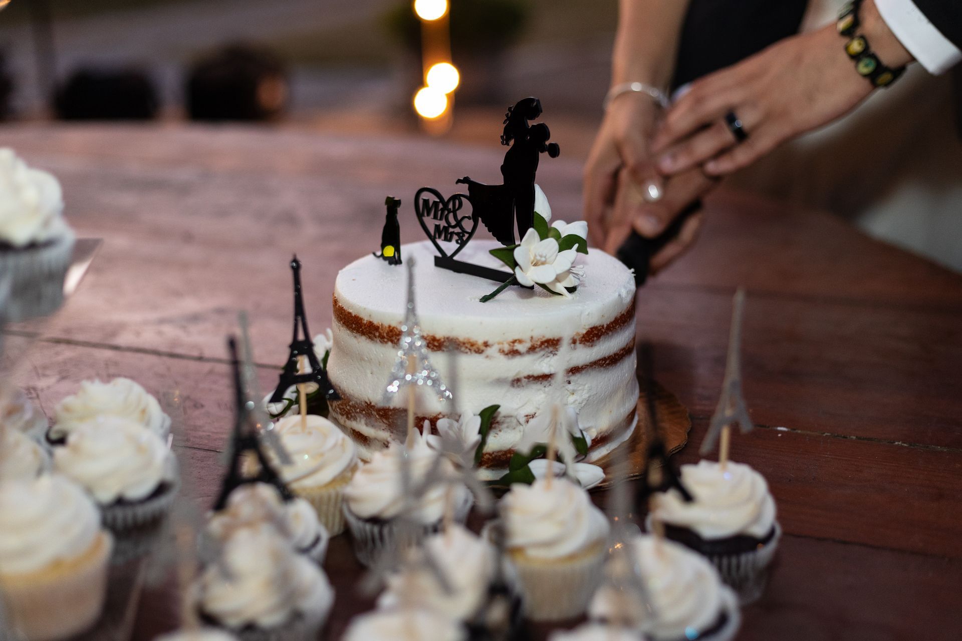 A bride and groom are cutting their wedding cake surrounded by cupcakes.