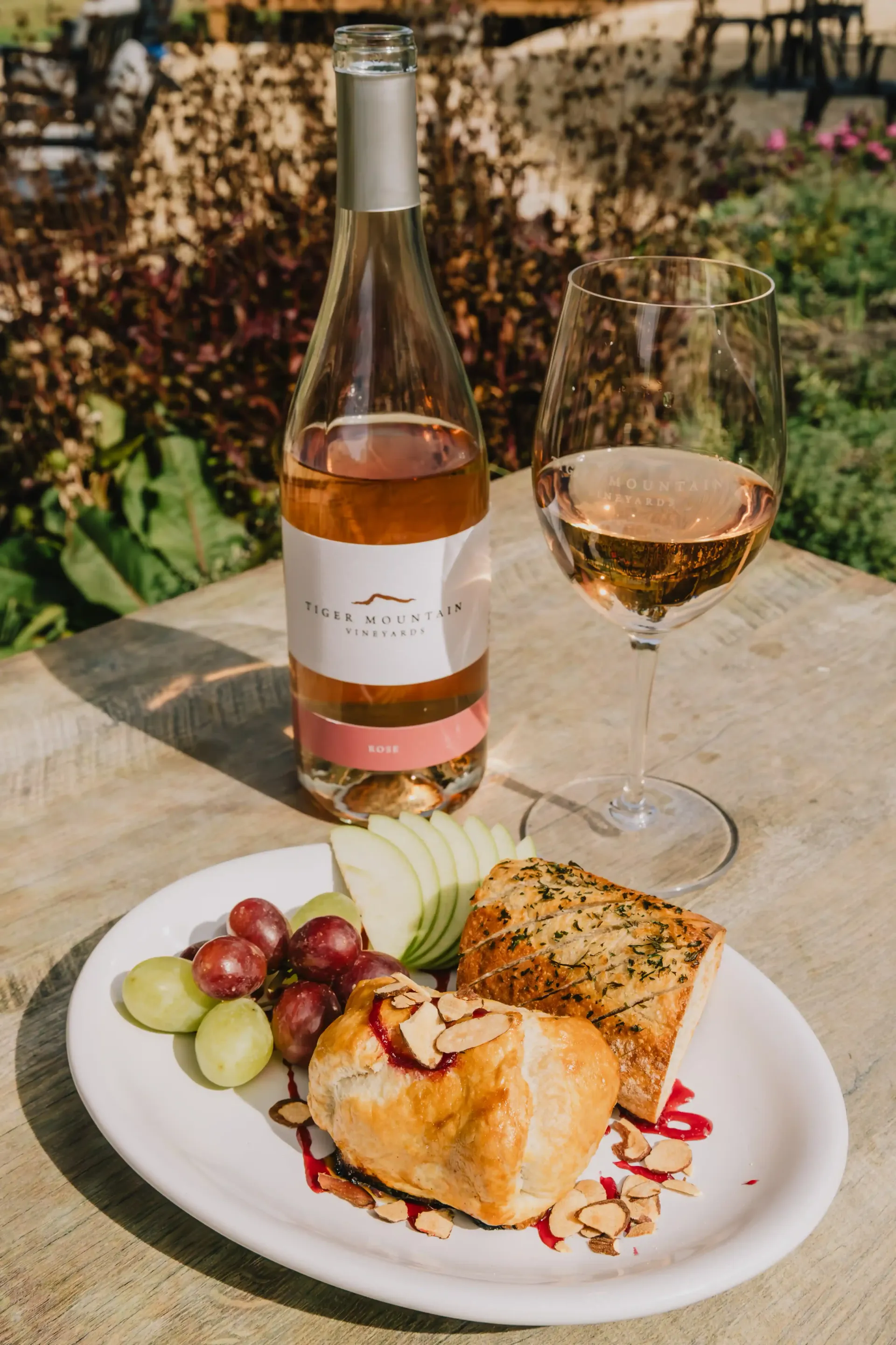 A bottle of wine and a glass of wine are on a table next to a plate of food.