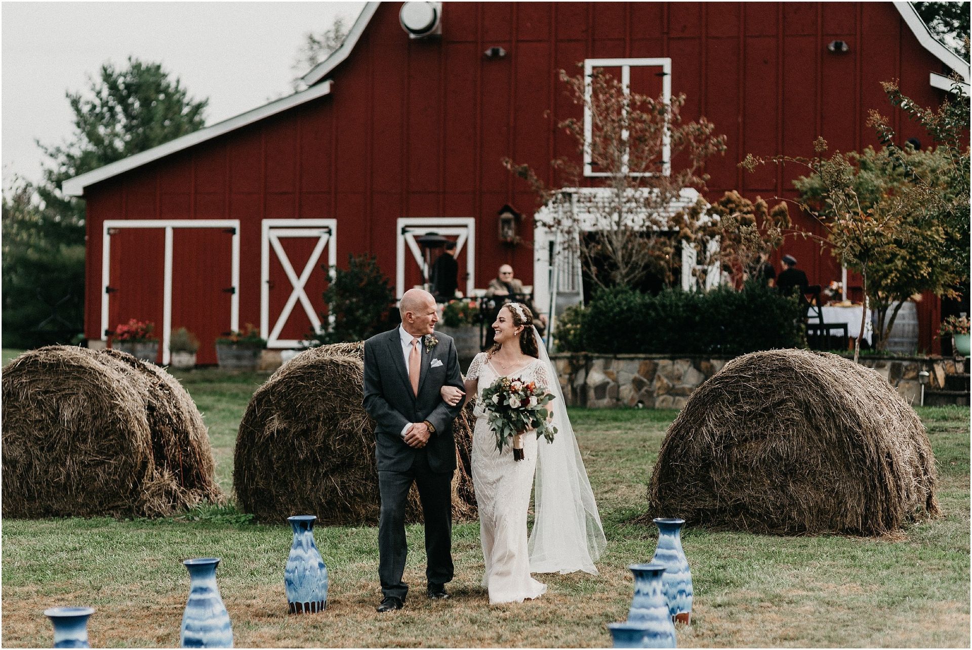A bride and groom are walking down the aisle in front of a red barn.