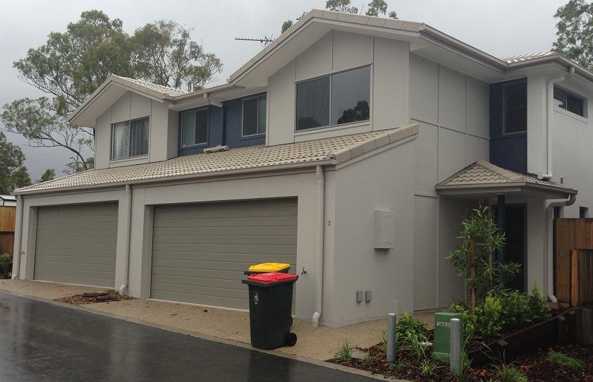A house with three garages and a trash can in front of it.