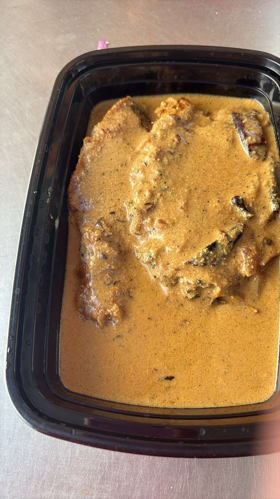 Black plastic container with a creamy orange-brown food dish and visible chunks on top.