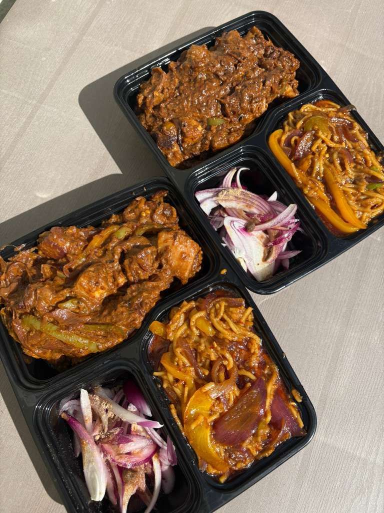 Three black takeout containers with saucy food, yellow garnish, and sliced red onions on a table