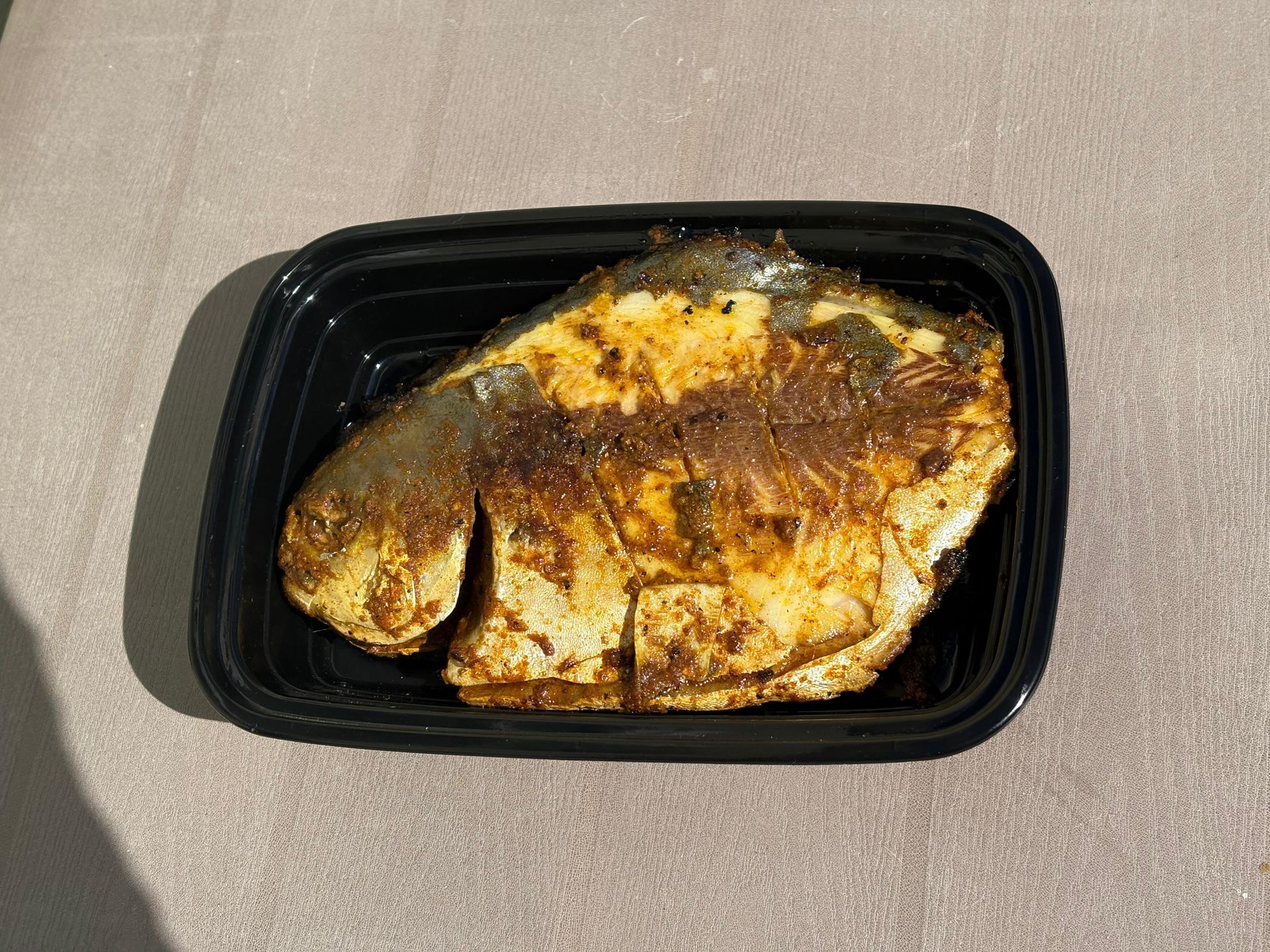 Grilled fish fillet in a black plastic tray on a light surface