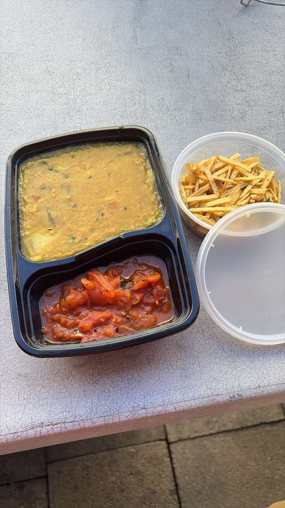 Takeout meal with soup, red saucy dish, and fries in plastic containers on a table