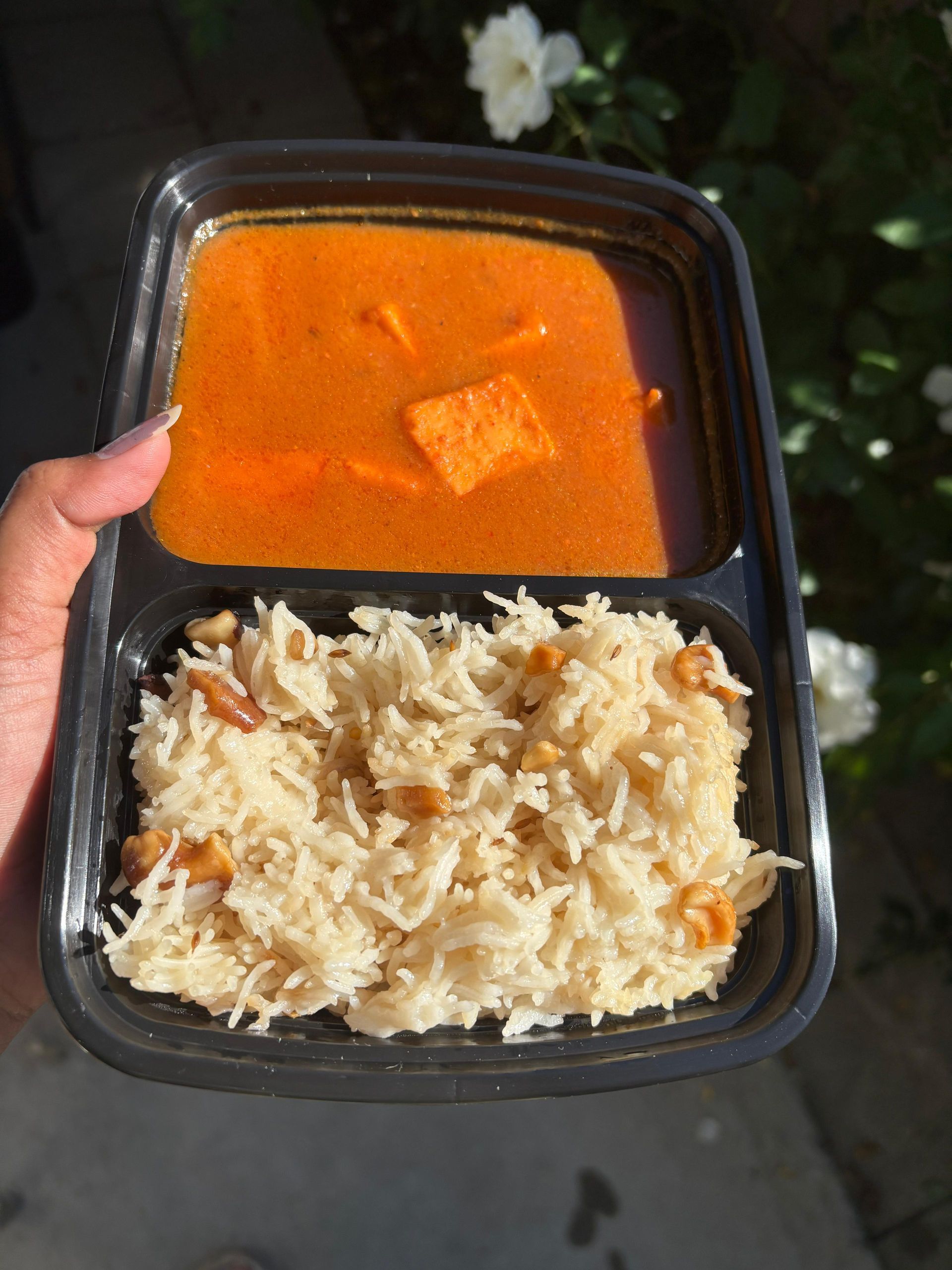 Takeout meal with rice and orange curry in a black container, held in one hand