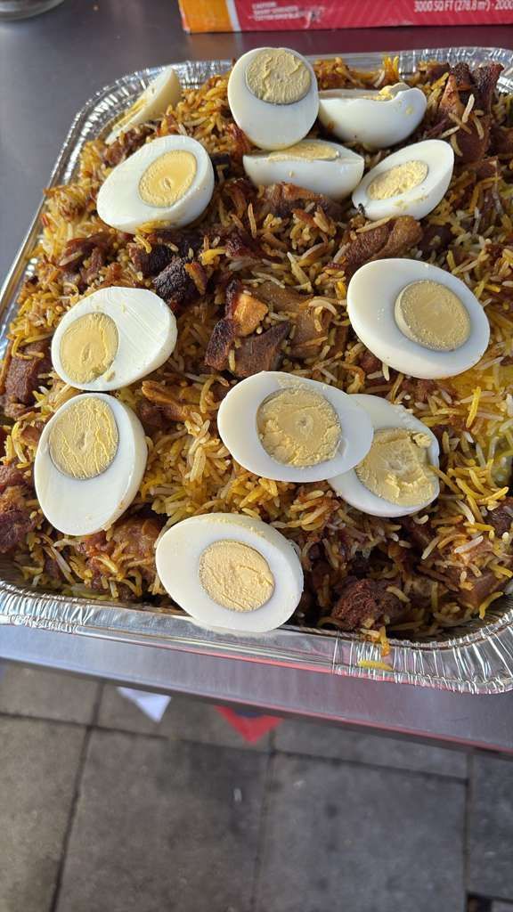 Foil tray of biryani topped with sliced hard-boiled eggs on a table.